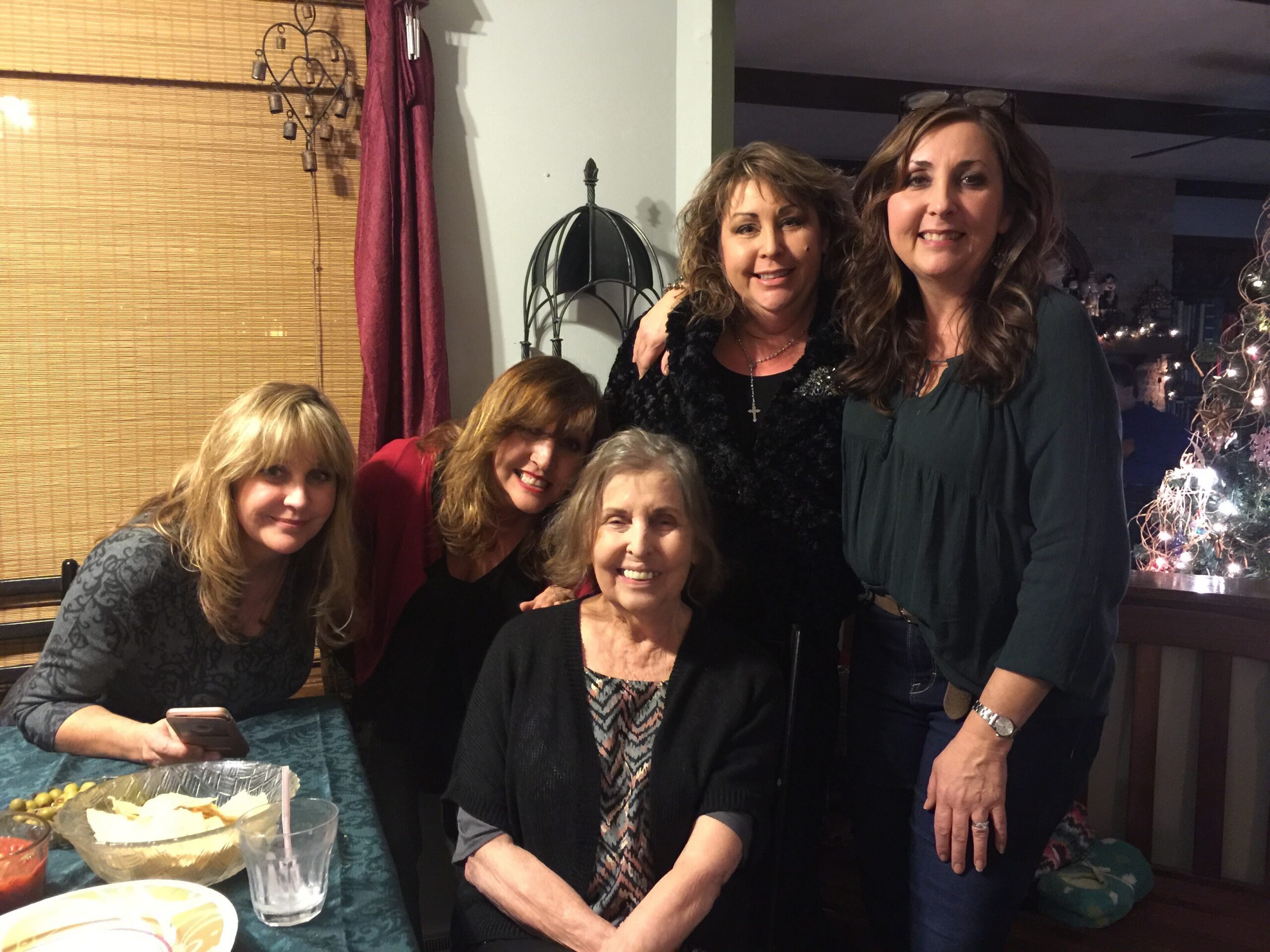 Group of smiling women posing for a photo at a party around a table with snacks and drinks in view.