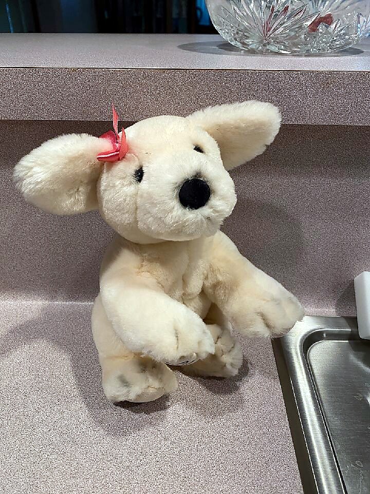 White plush dog toy with a pink bow sits on a glittery pink kitchen counter by a sink.