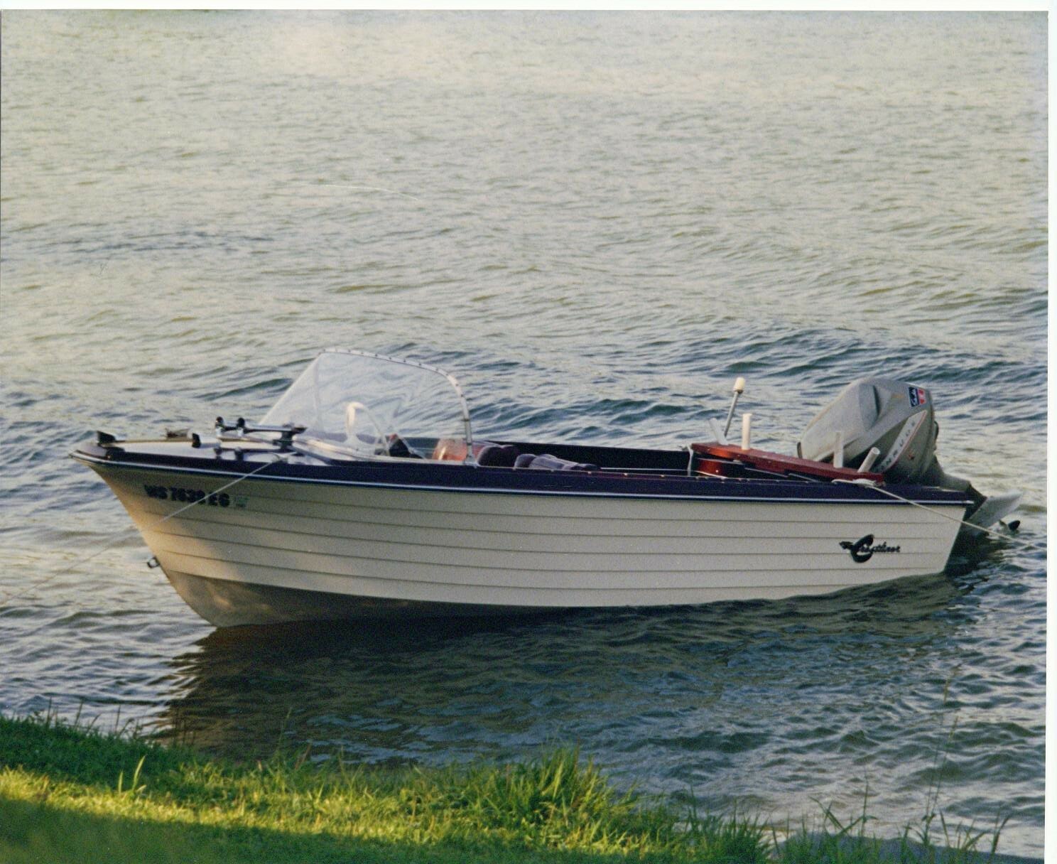 Small white motorboat with a windshield floating near grassy shore on calm water.
