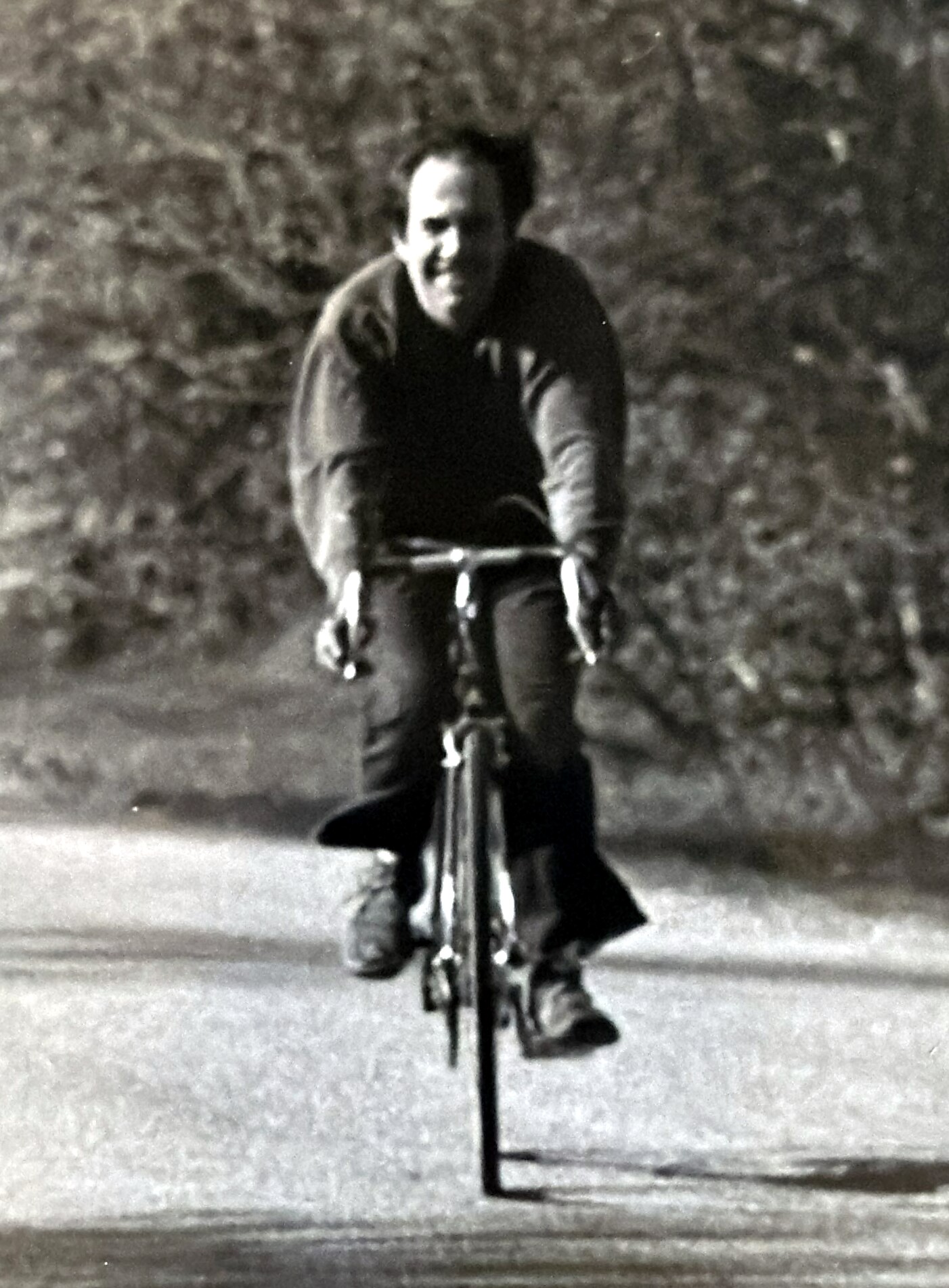 Man cycling toward the viewer on a road; black-and-white photograph.