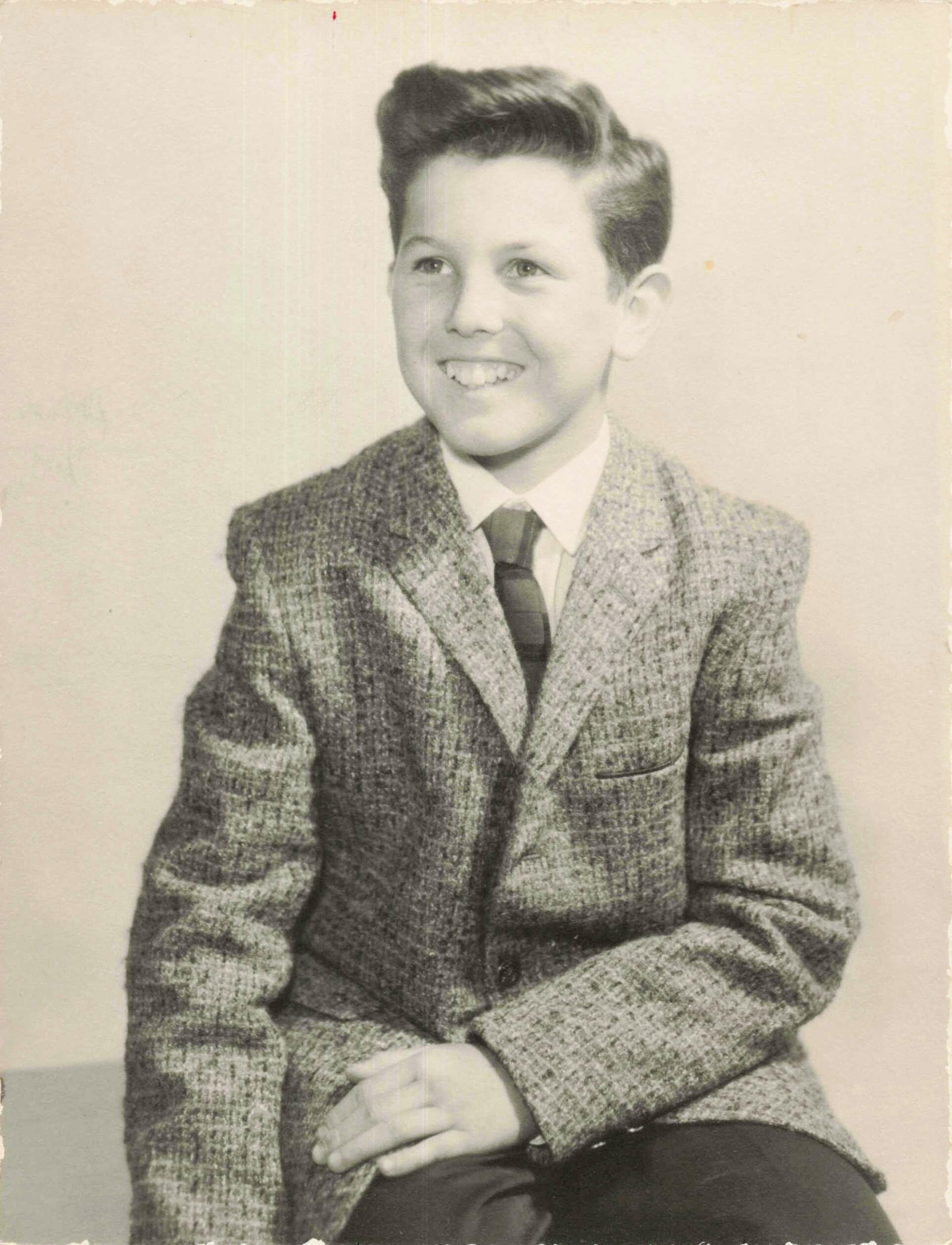 Young man in a checked blazer and tie, seated, smiling toward the left.