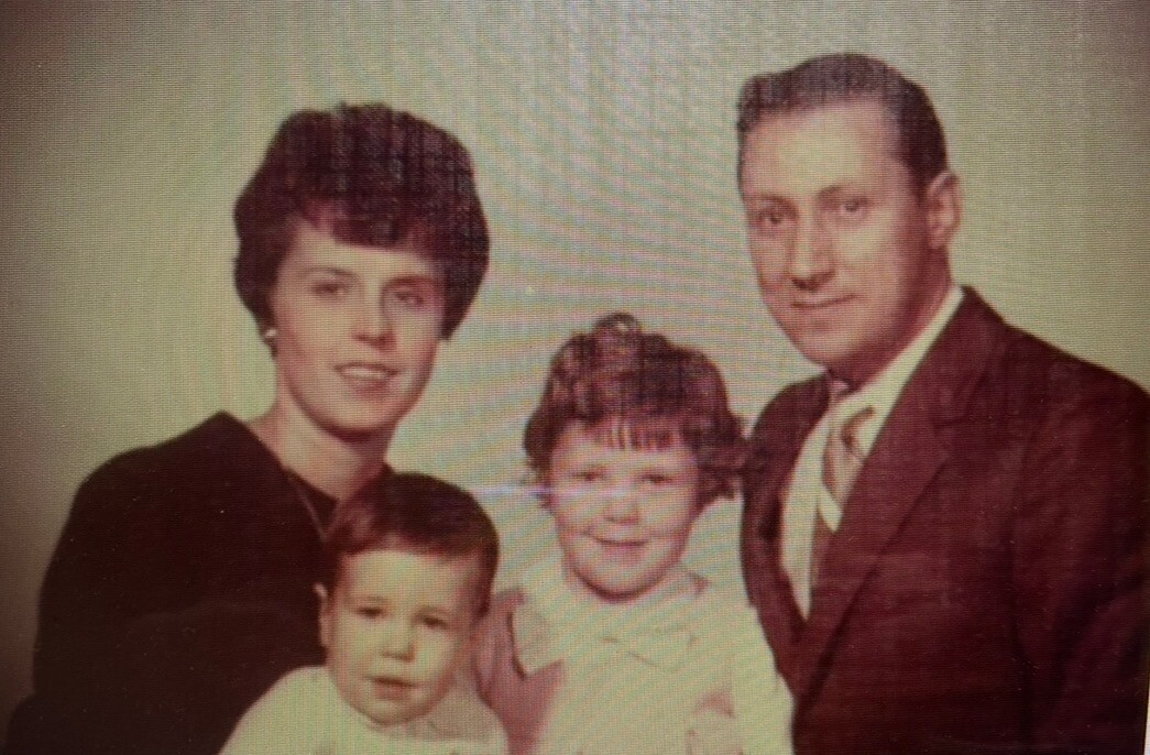 Family of four posing for a formal portrait: mother on the left, father on the right, with a young boy in front left and a girl in the center smiling between them.