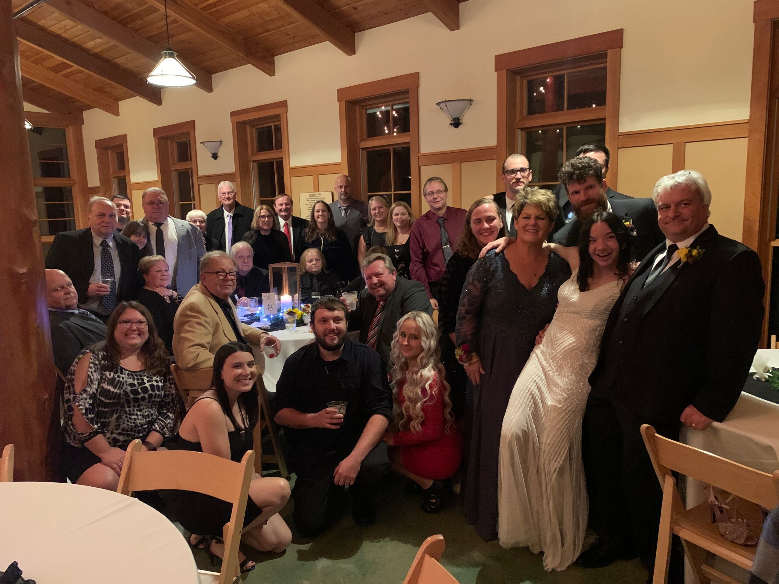 Large group of wedding guests posing for a photo at a reception, with a bride in a white gown and groom in a suit in the foreground.