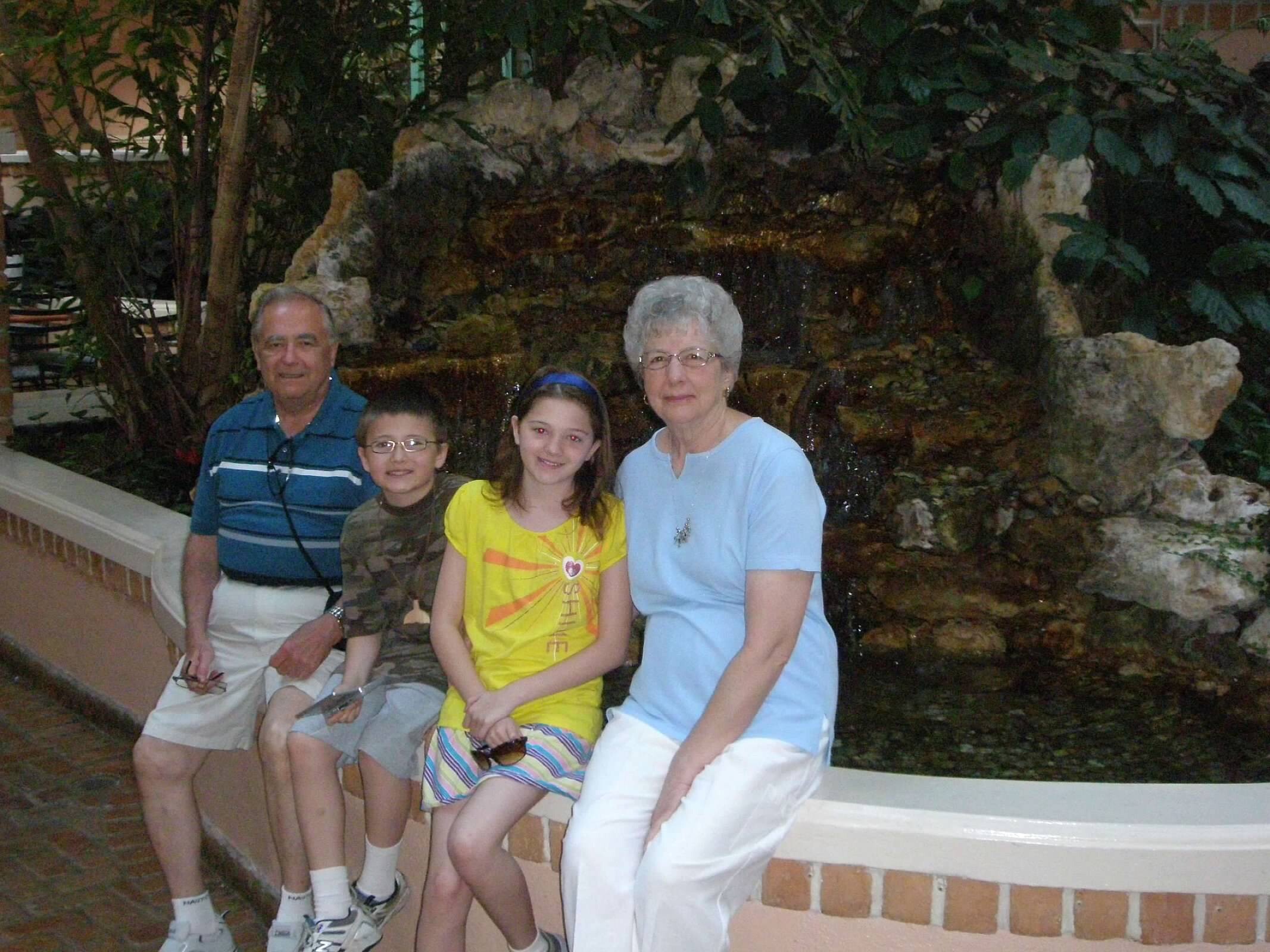A family of four posing together outdoors in front of a rocky fountain on a brick ledge.