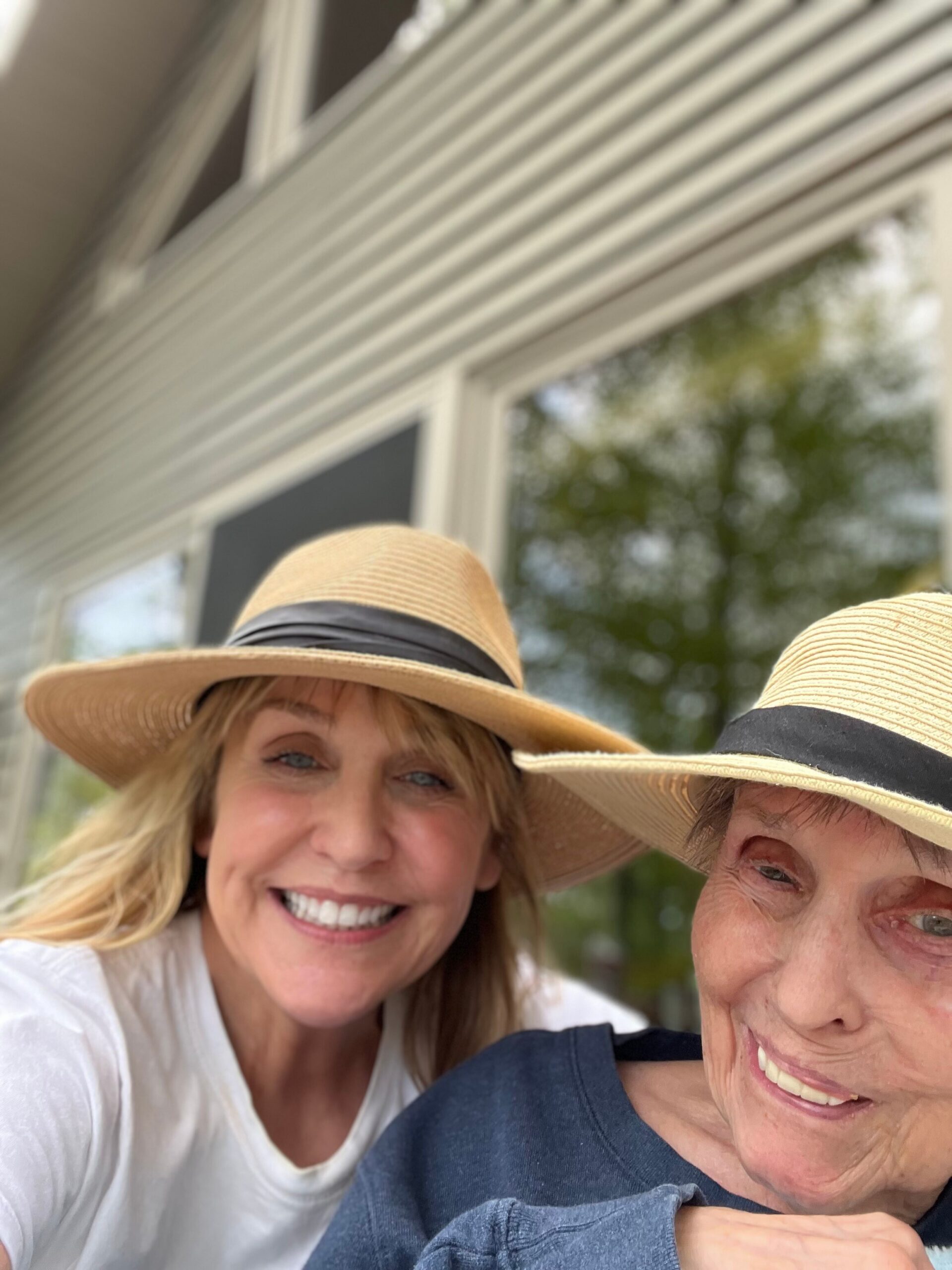 Two women wearing wide-brimmed straw hats posing for a sunny outdoor selfie, smiling at the camera.