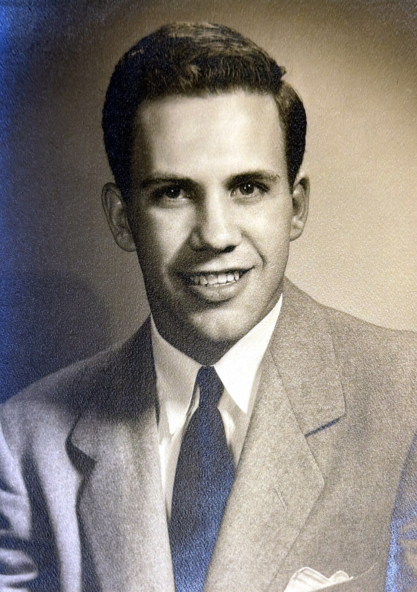 Young man in a suit and tie smiling in a studio portrait, cropped at chest height.
