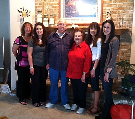 Six adults smiling for a group photo in a living room, standing by a brick fireplace.