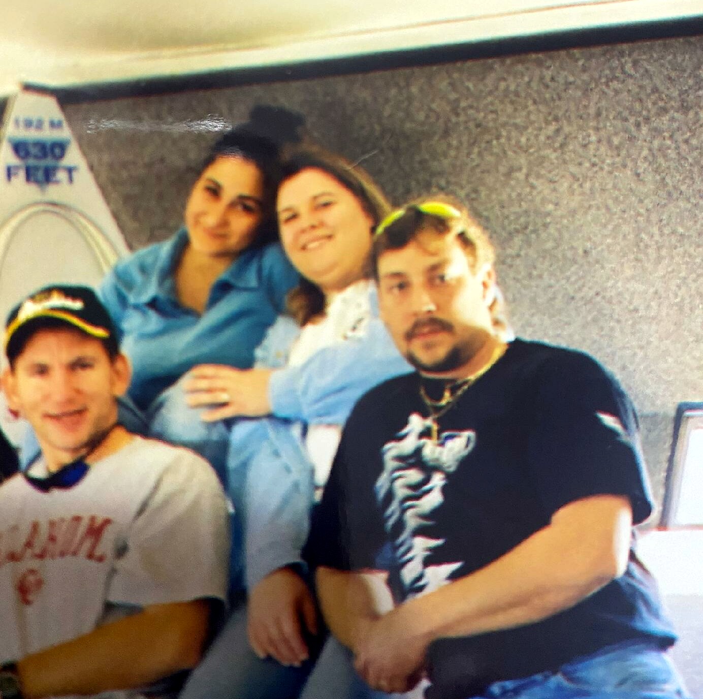 Three men sit close together on a bus, smiling at the camera in a casual group photo.