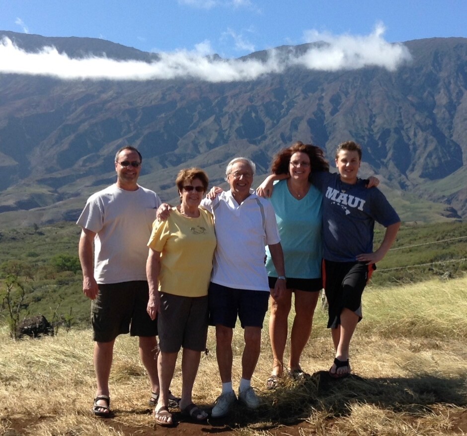 Five people pose together on a sunny hillside with a mountain range behind them.”],