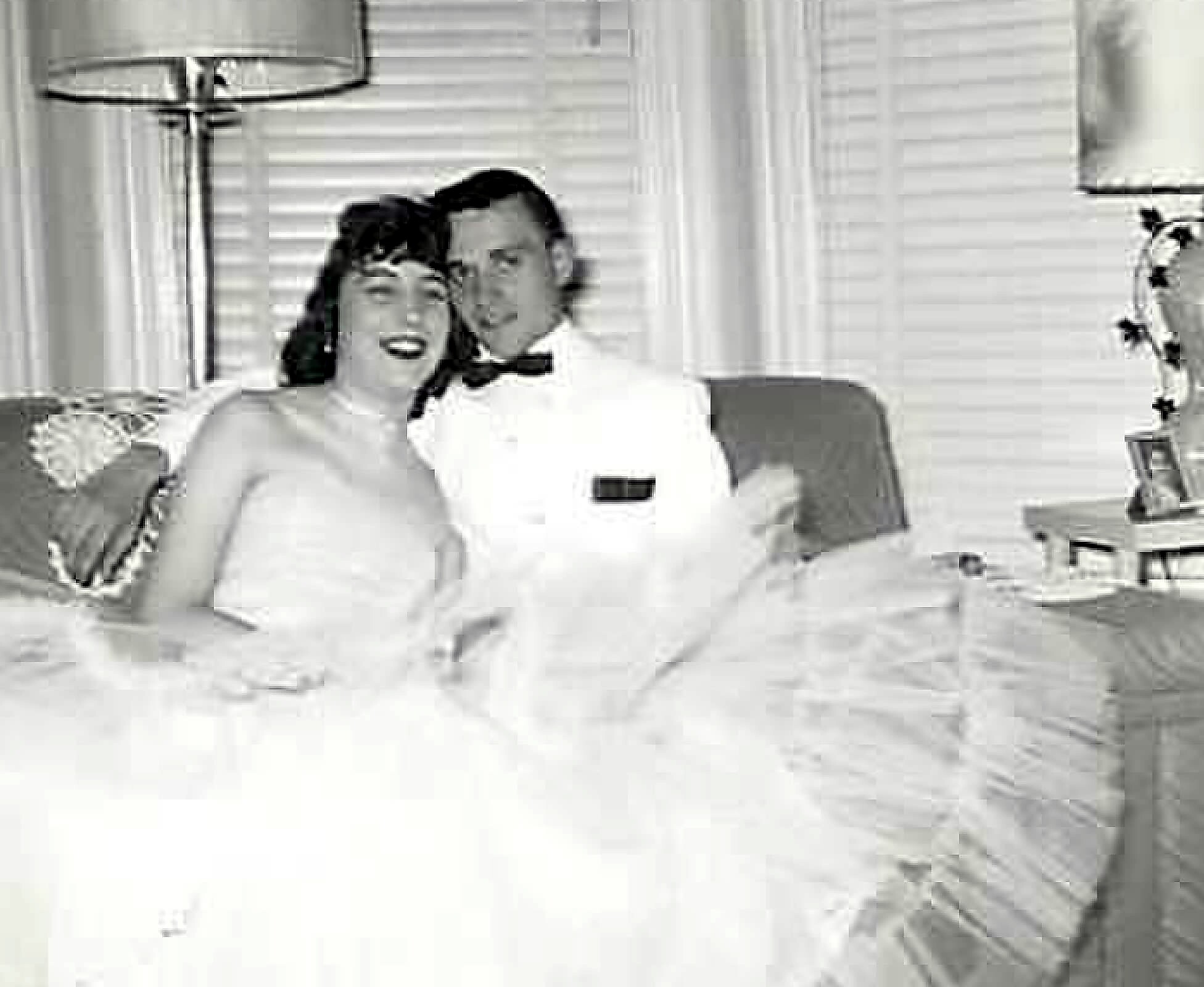 Smiling couple sitting close together on a sofa in a living room with a floor lamp behind them.