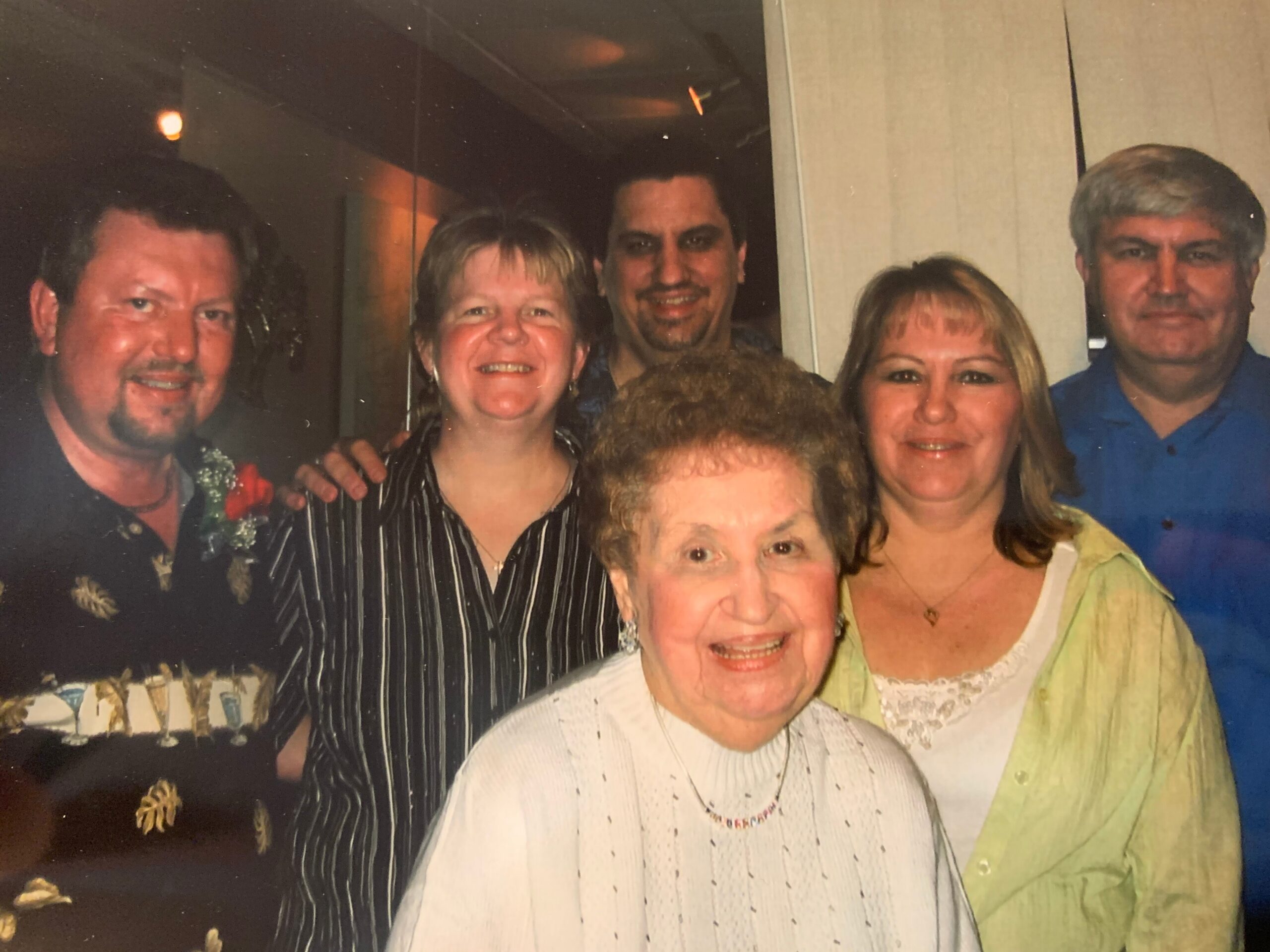 Group of five adults smiling for a photo at a social gathering indoors.