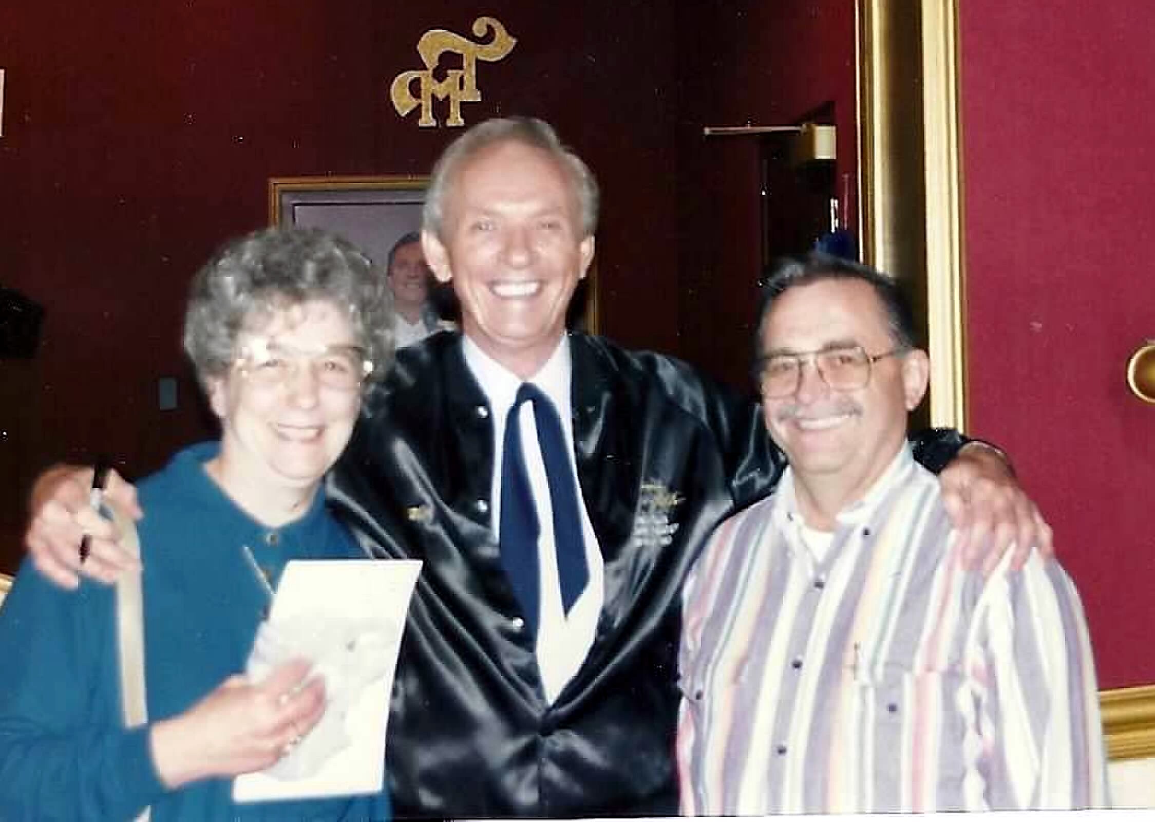 Three adults posing together at a celebration, smiling for the camera against a burgundy background.