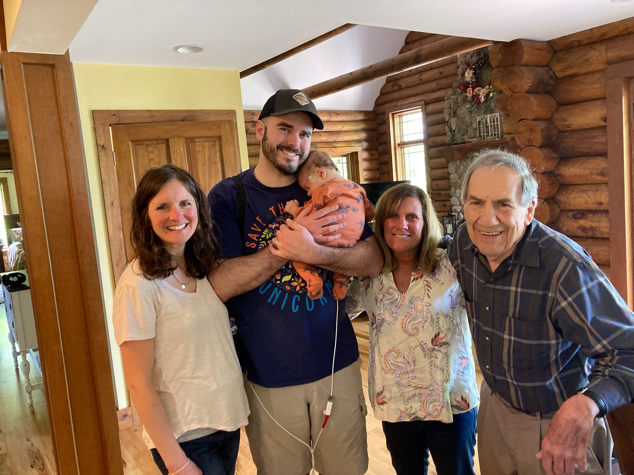 Smiling family group in a log cabin, with a man holding a baby in the center.