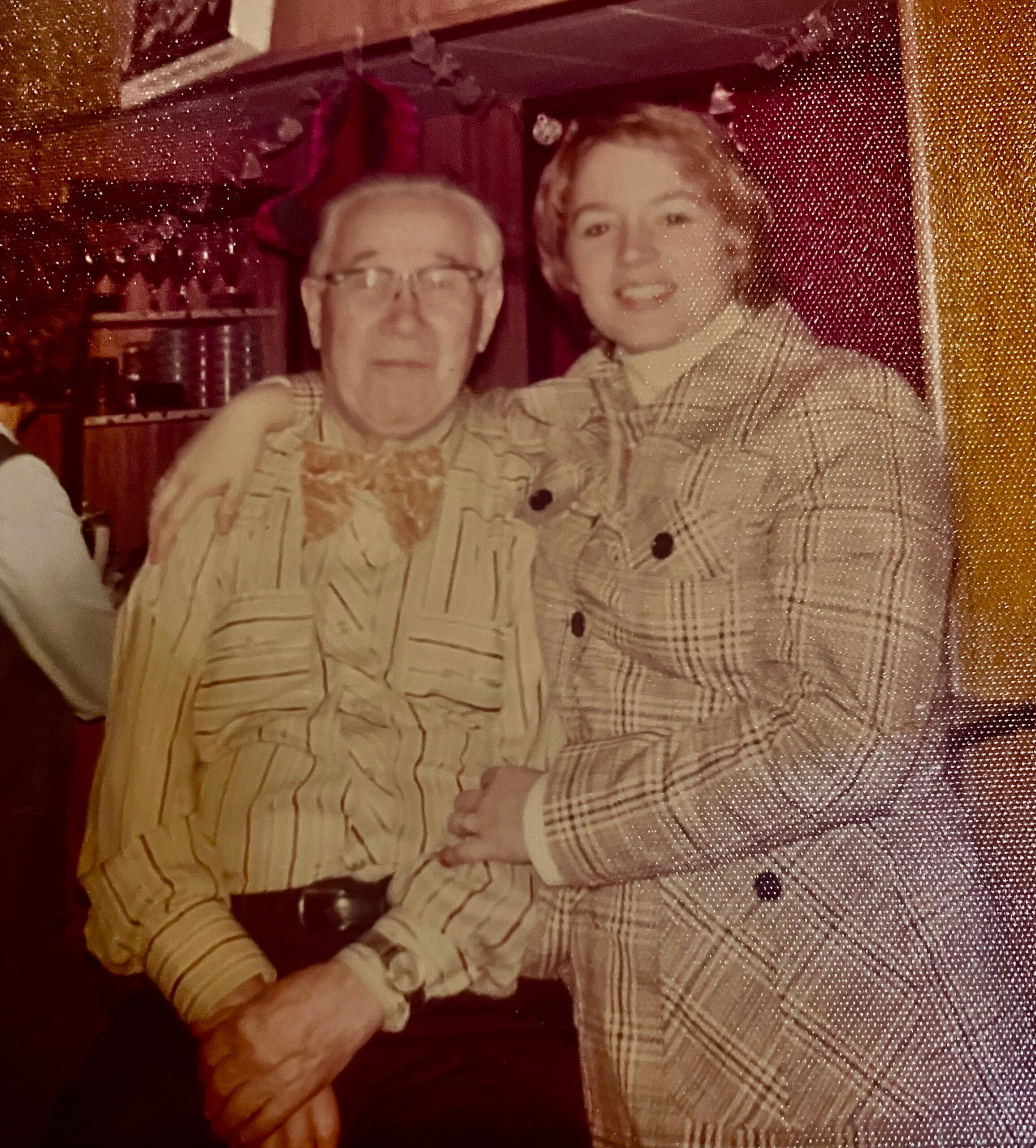 Older man with glasses in a striped shirt posing with a smiling woman in a plaid shirt indoors.