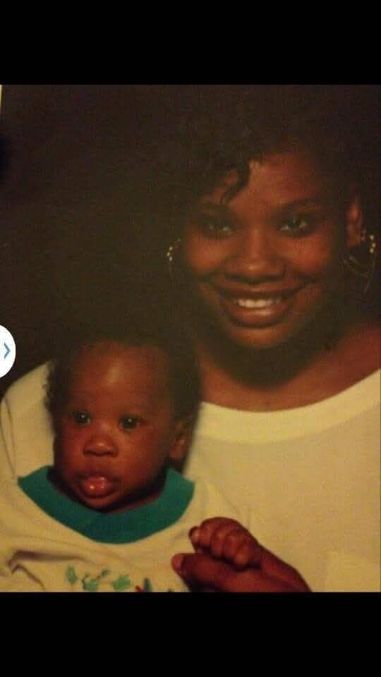 African American woman smiling while holding a baby; both look at the camera.