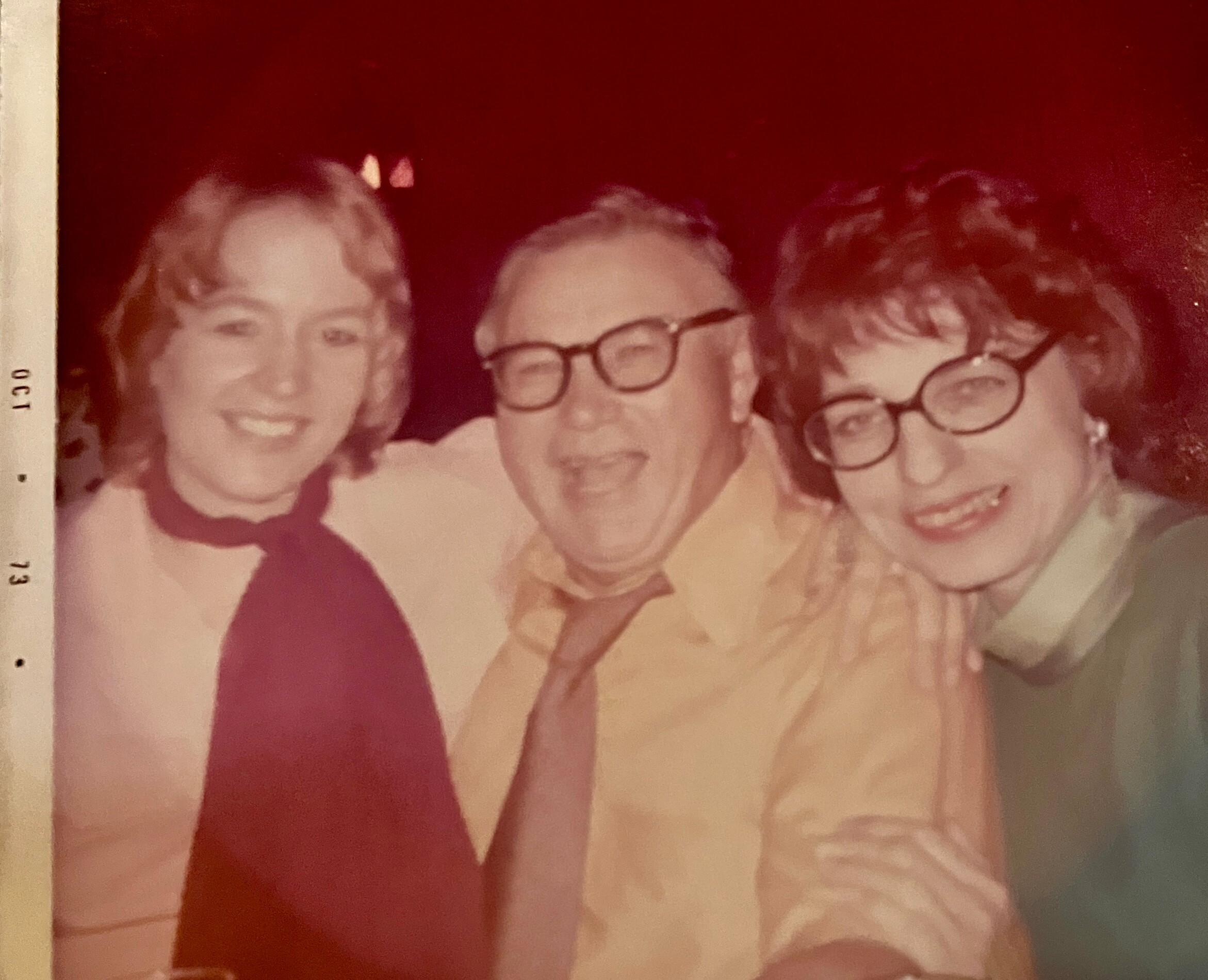 Three people posing closely for a group photo, all smiling; two are wearing glasses.