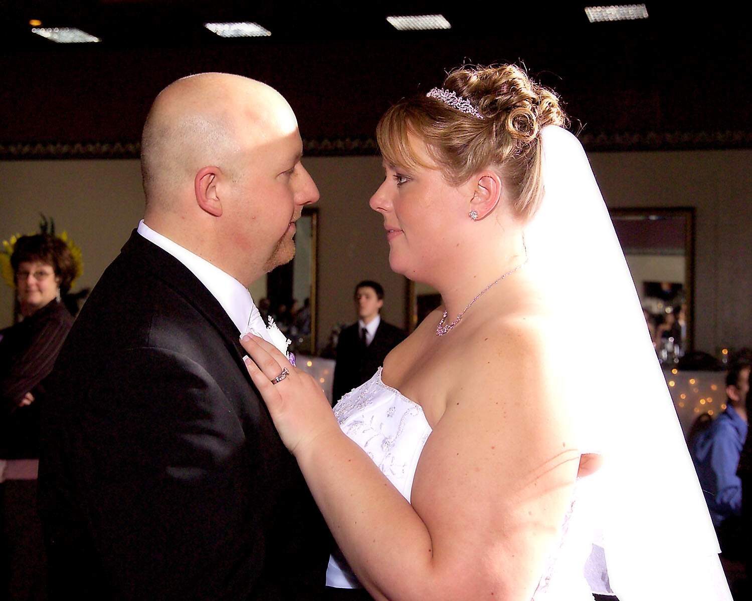 Bride and groom facing each other at their wedding, preparing to kiss in a dimly lit reception hall.