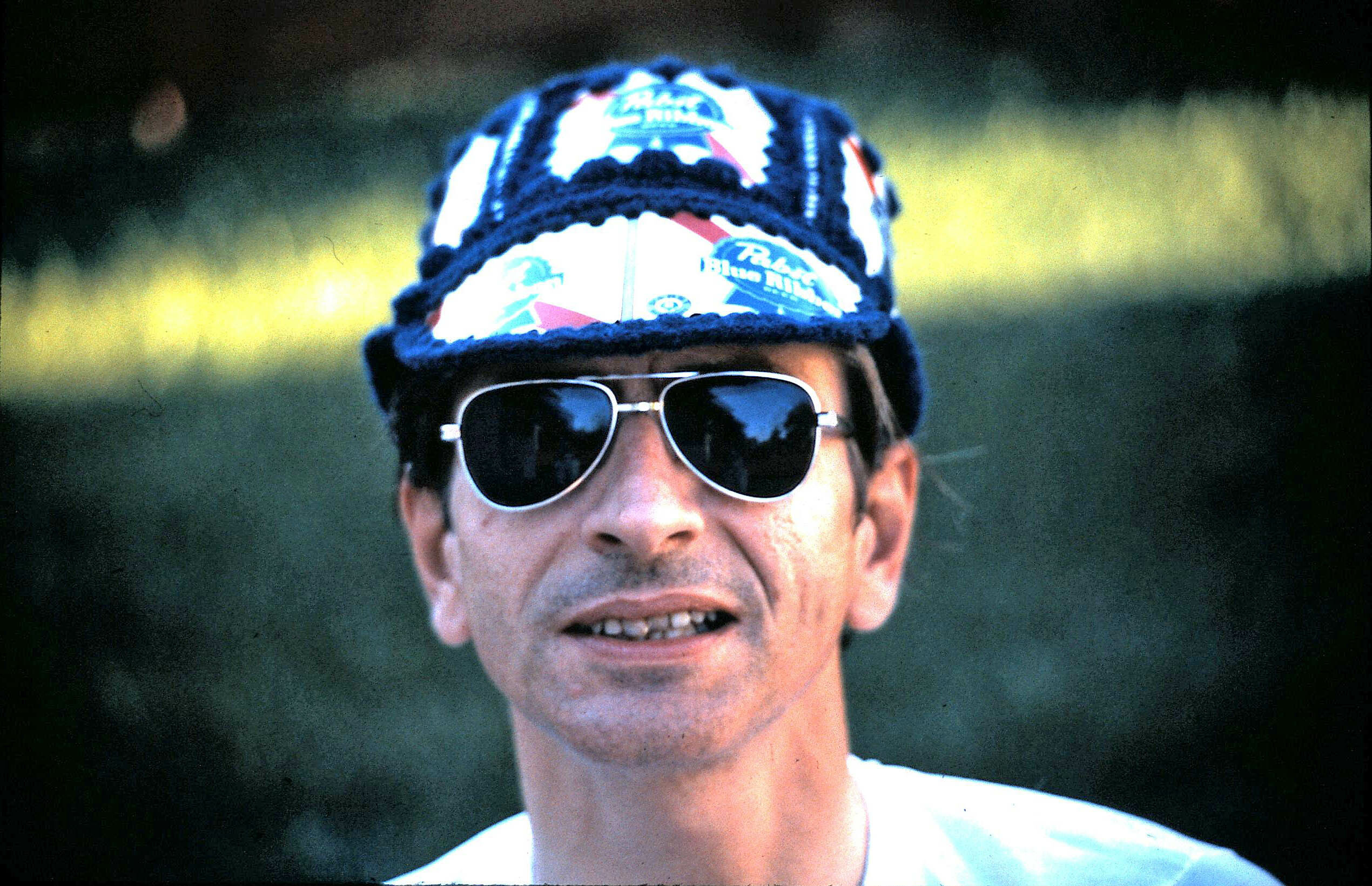 Man wearing dark aviator sunglasses and a knit cap with colorful patches, outdoors.