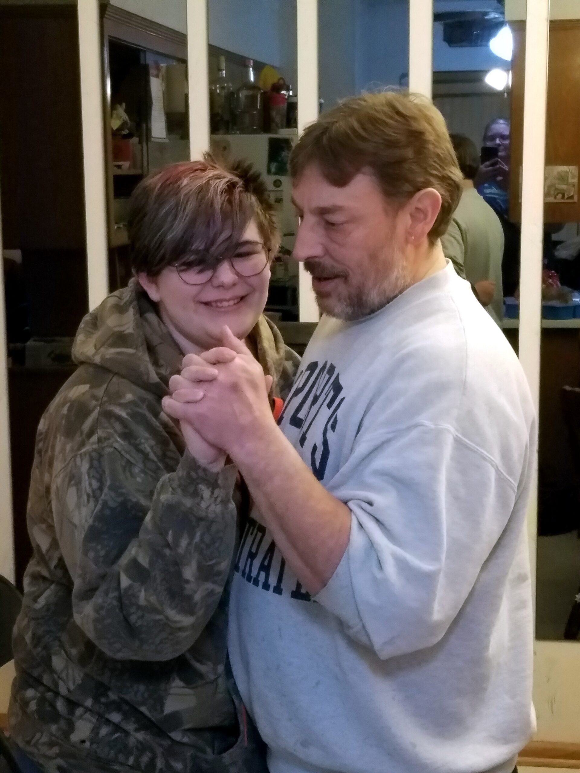 A man and a woman dancing closely indoors, holding hands and smiling at the camera.
