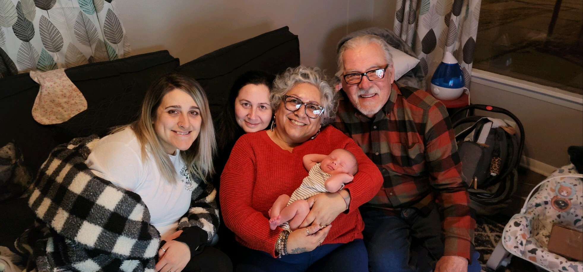 Smiling family of five on a couch with a newborn baby, cozy living room setting.