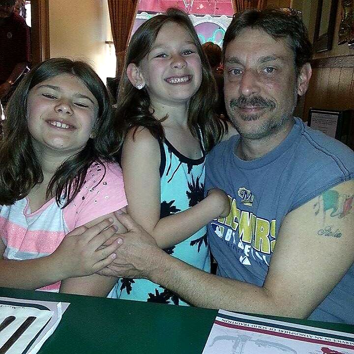 Man and two young girls smiling at the camera while seated at a restaurant table, arms around each other.
