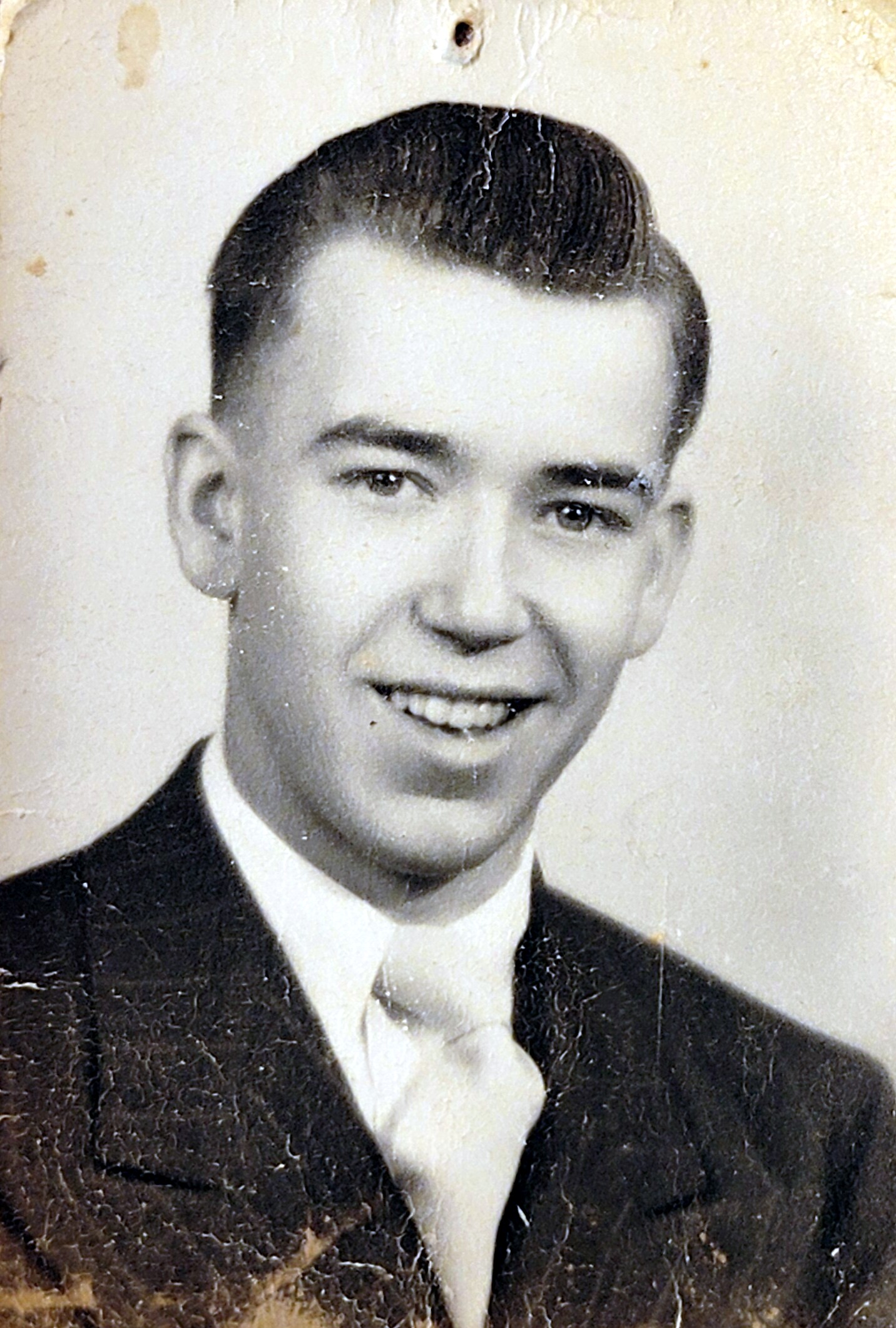 Black-and-white portrait of a smiling young man in a suit and tie, looking at the camera.