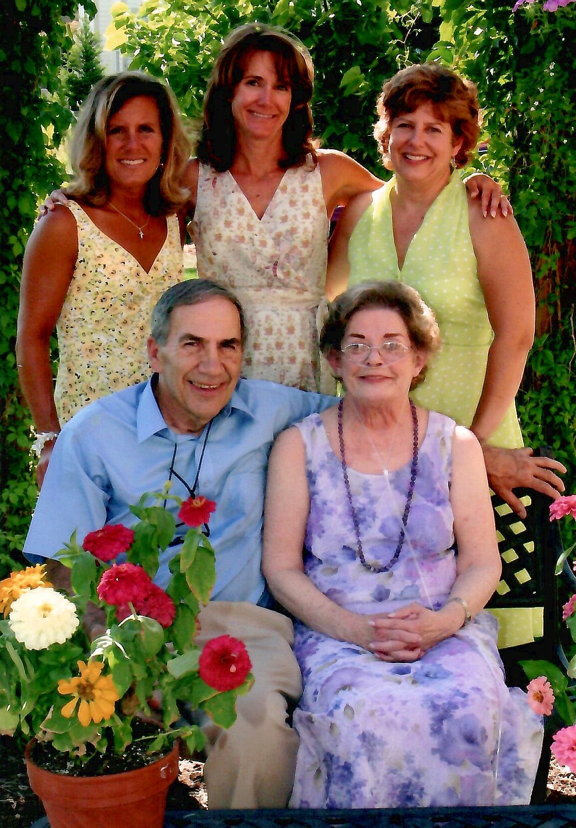 Five adults posing in a sunny garden with colorful flowers, smiling at the camera.