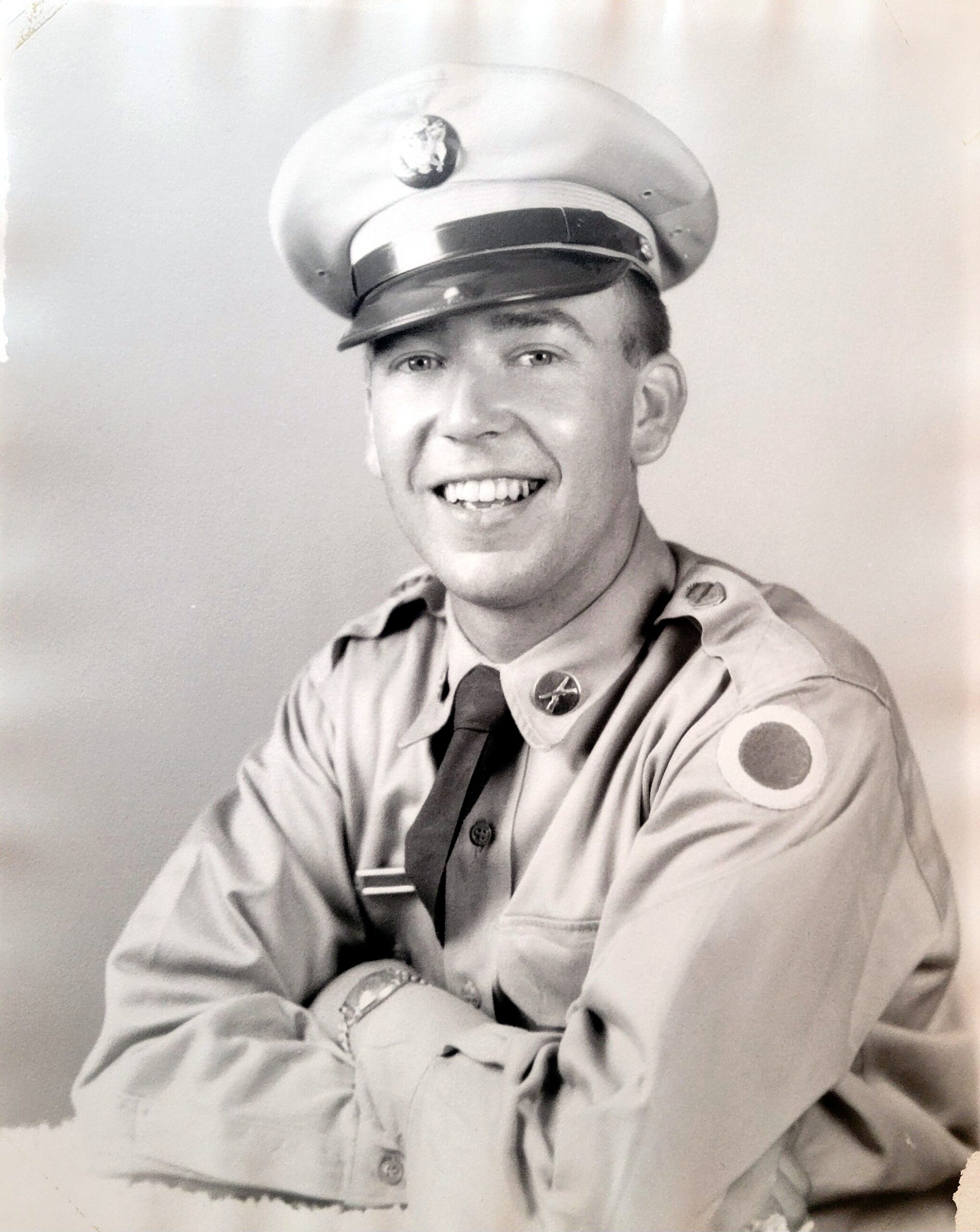 Smiling young man in a vintage military uniform with cap and tie, studio portrait.