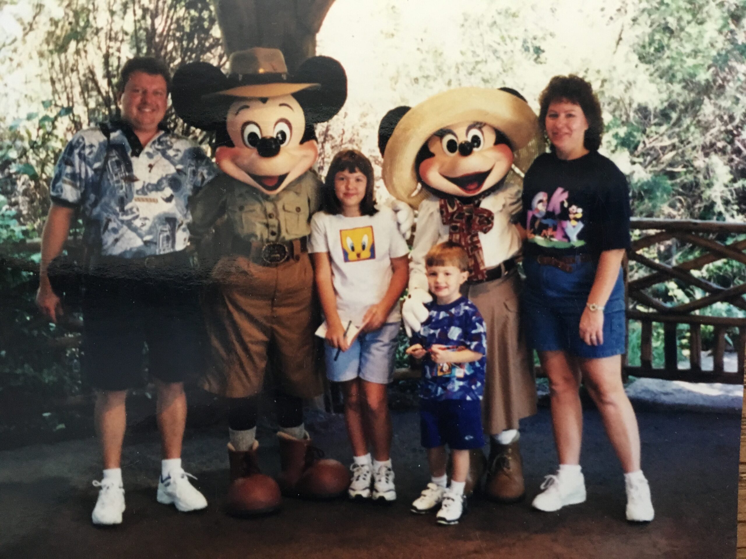 Family posing with Mickey and Minnie Mouse mascots at an outdoor theme park