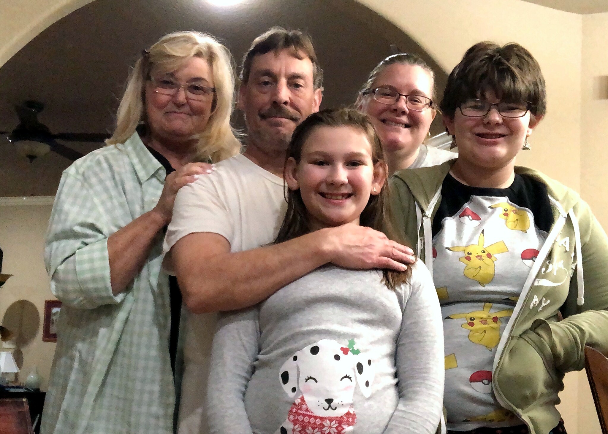 Five people pose closely for a warm group photo indoors, smiling at the camera.