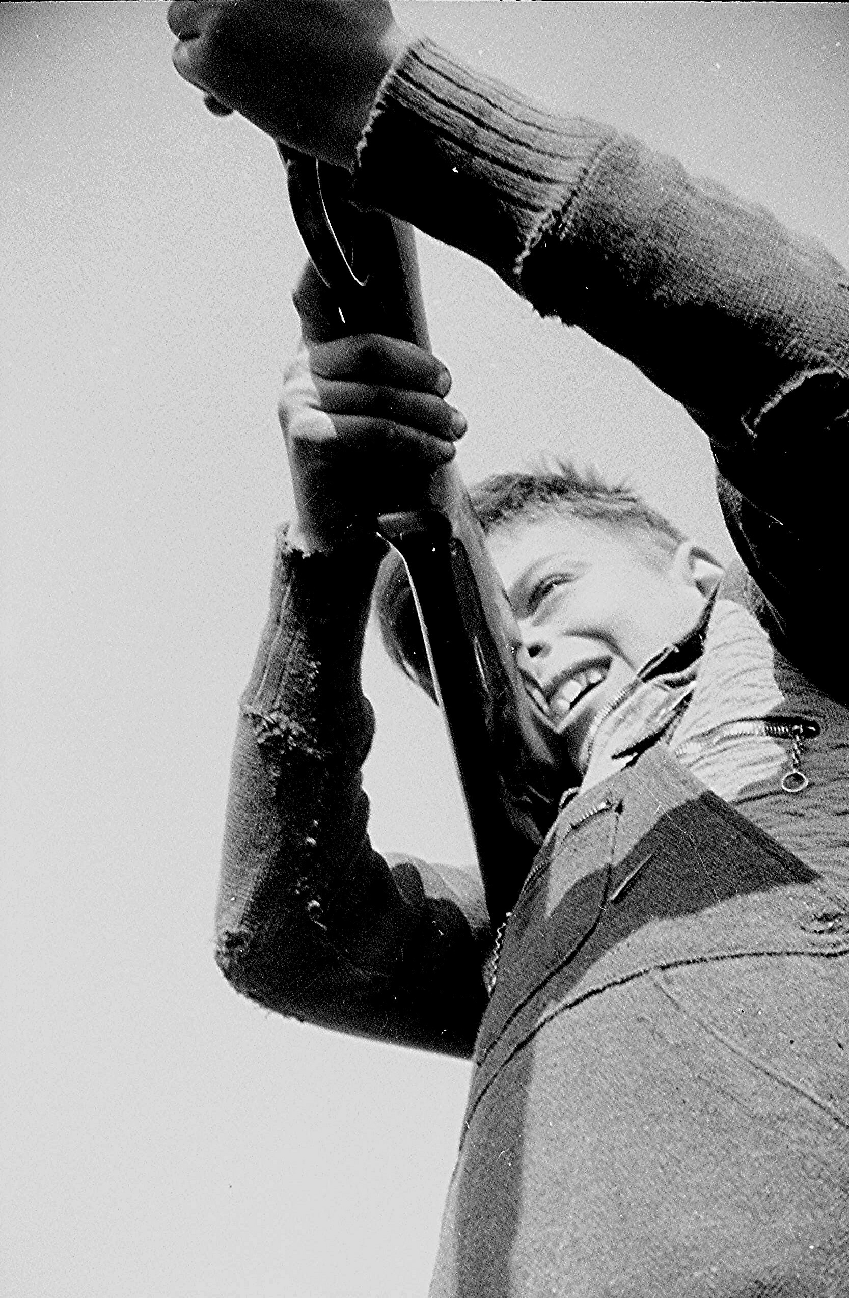 Smiling person raising the neck of an electric guitar in a black-and-white close-up shot.