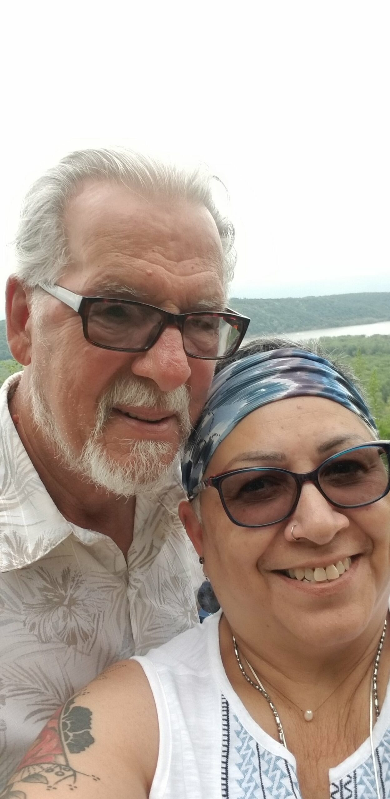 Smiling older couple taking a selfie outdoors on a hillside with a river in the background