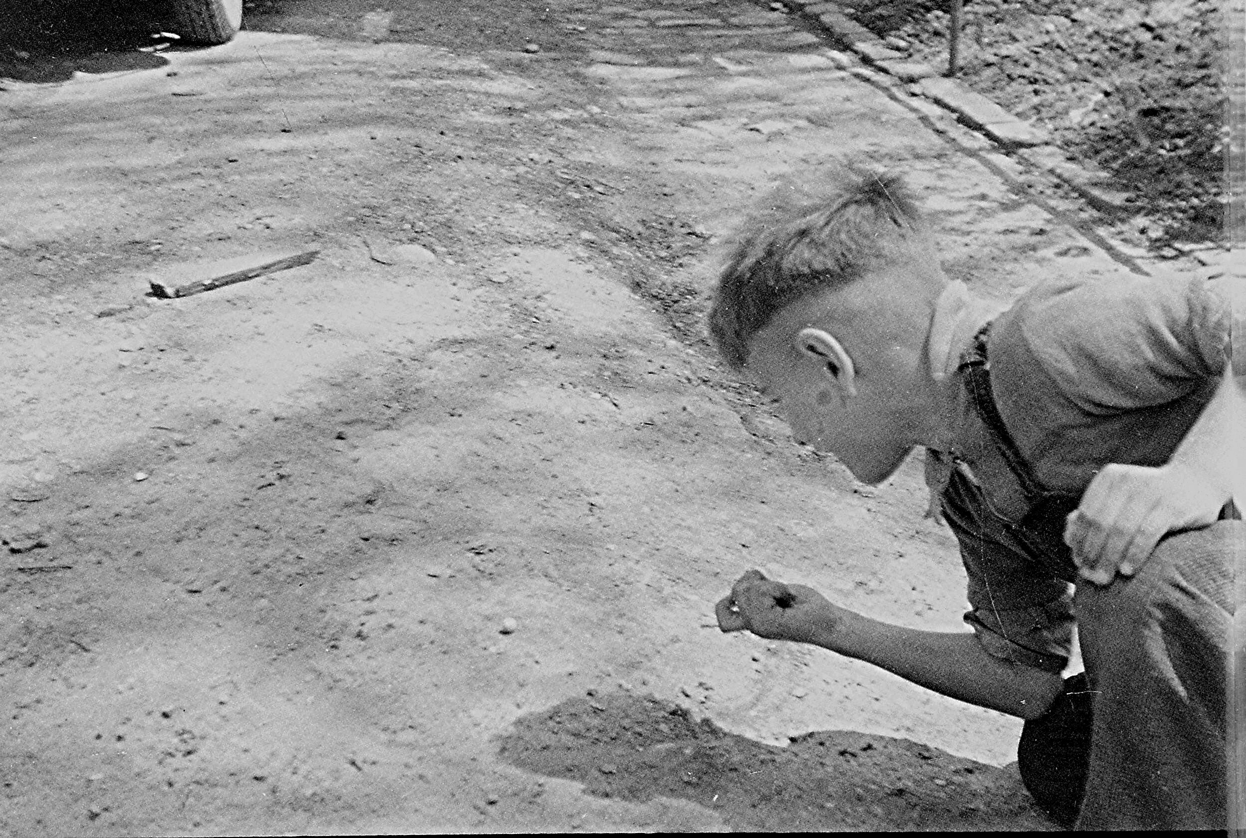 Child crouching in dirt outdoors, looking at a small object in their hands.