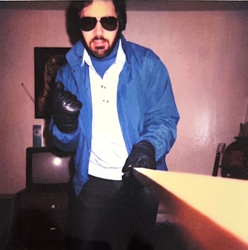 Man in sunglasses and a blue jacket points a glowing orange beam toward the camera indoors.”] ,