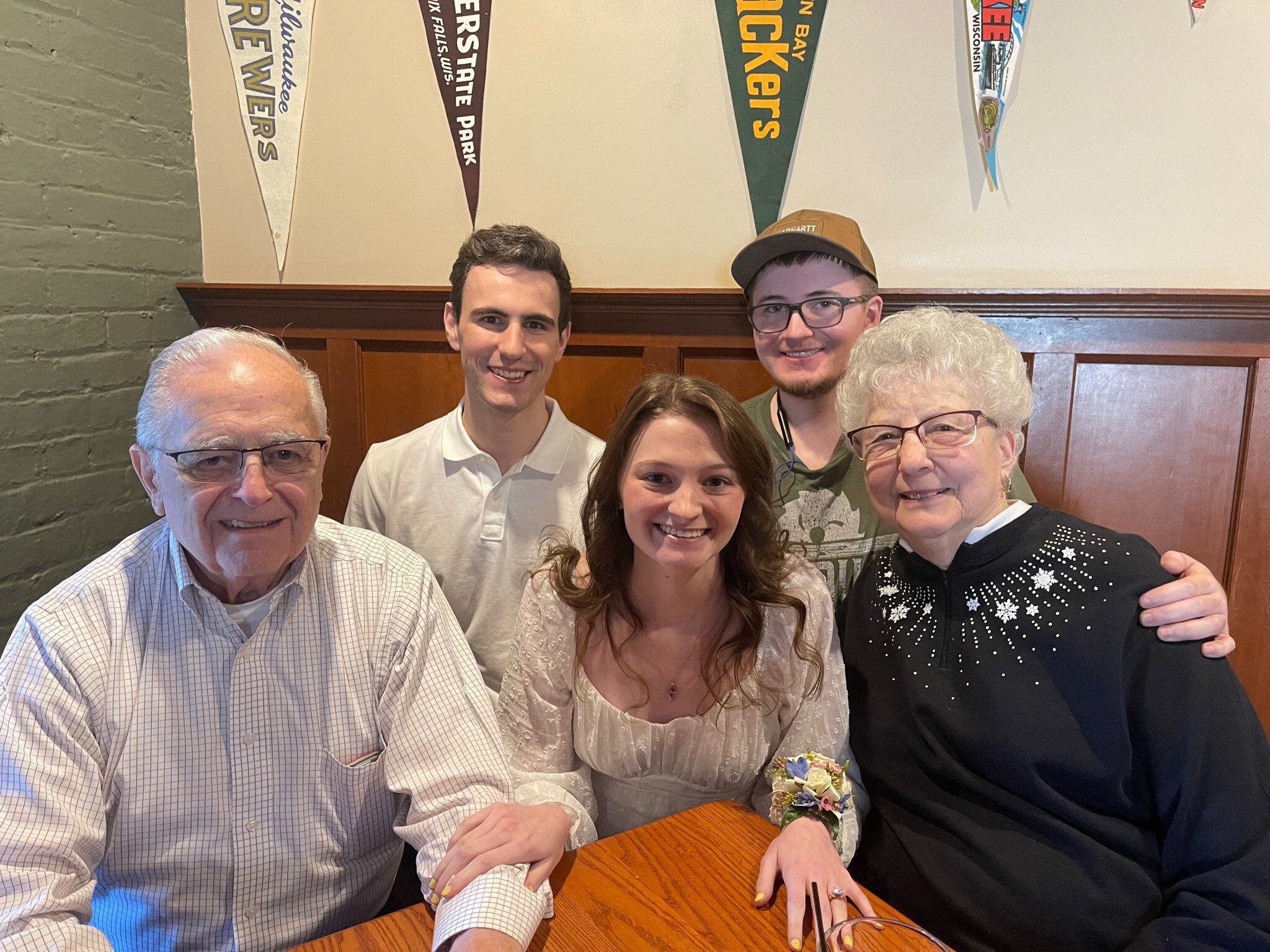 Six people gathered around a wooden table in a restaurant, smiling at the camera for a group selfie.