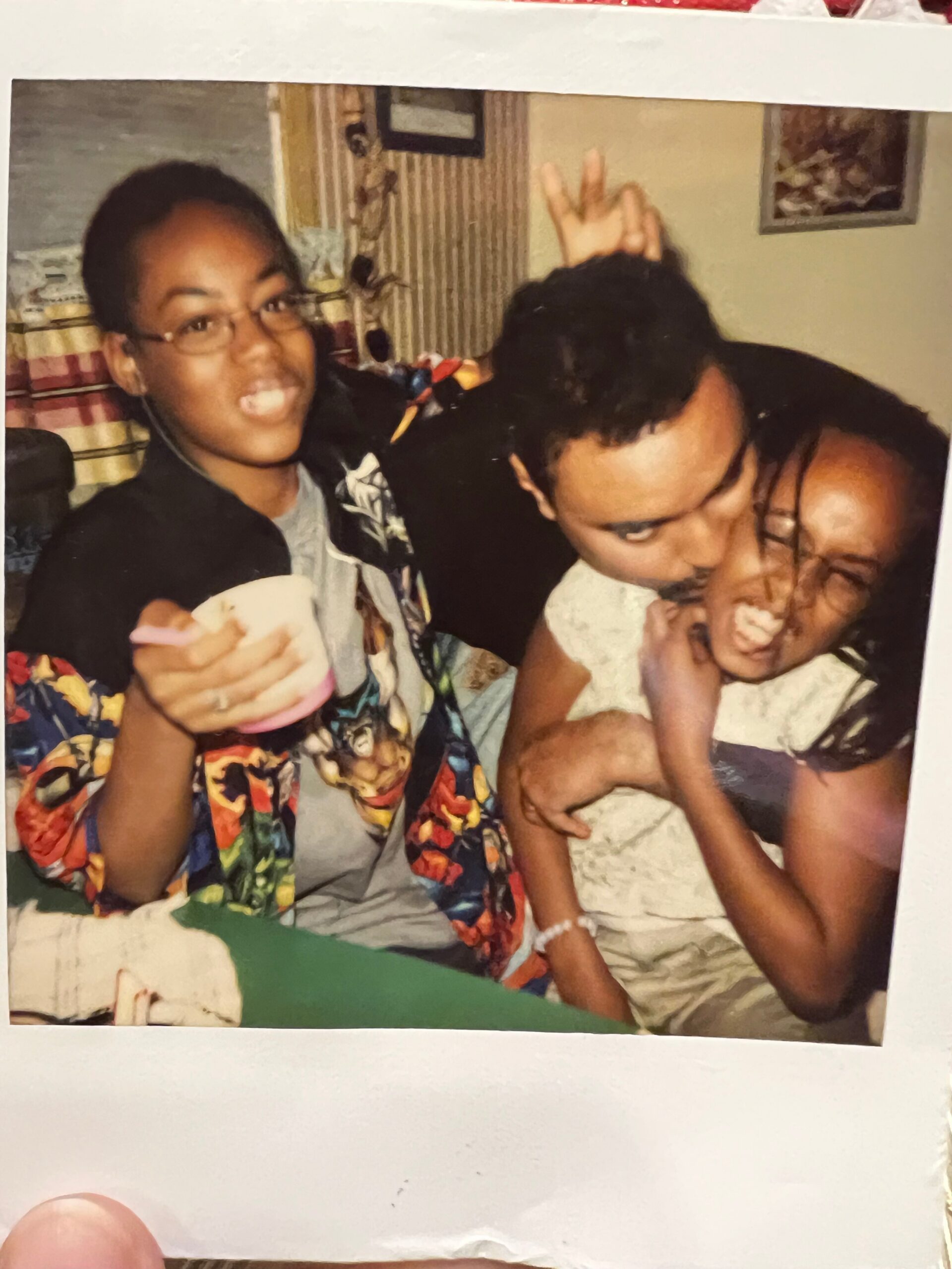 Woman with glasses smiling and pointing at the camera, flanked by two friends in a playful indoor photo.