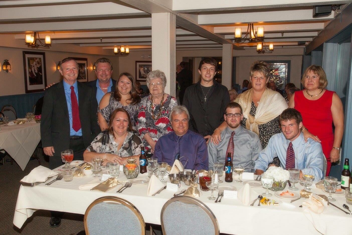 Group of ten adults posing for a photo around a banquet table at a formal dinner event in a function room.