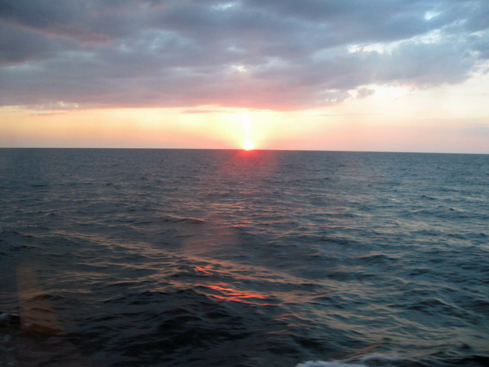 Sunset over a calm ocean with a colorful sky and scattered clouds on the horizon.