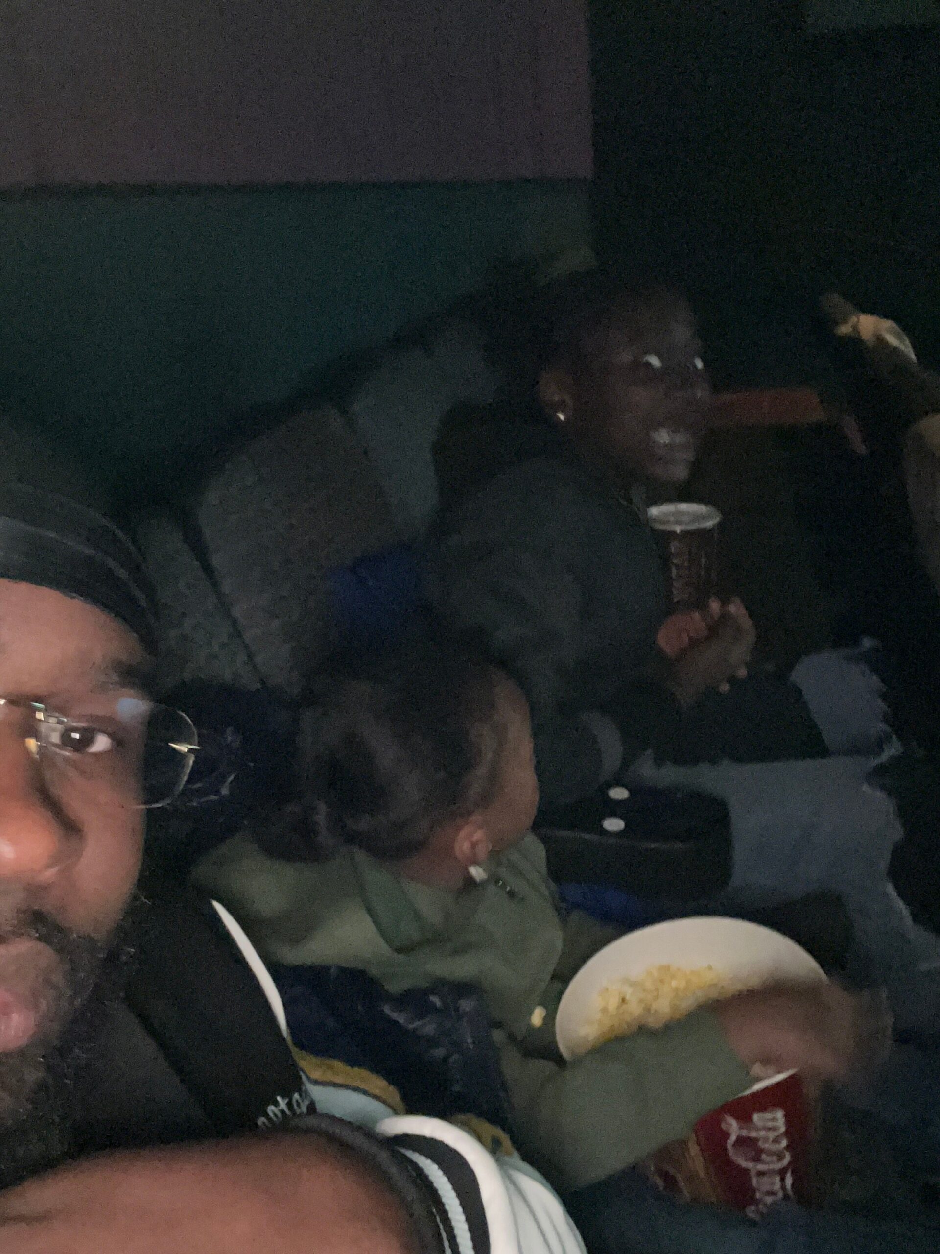 People riding in a dimly lit car at night, snacking on popcorn and drinks in the back seat.
