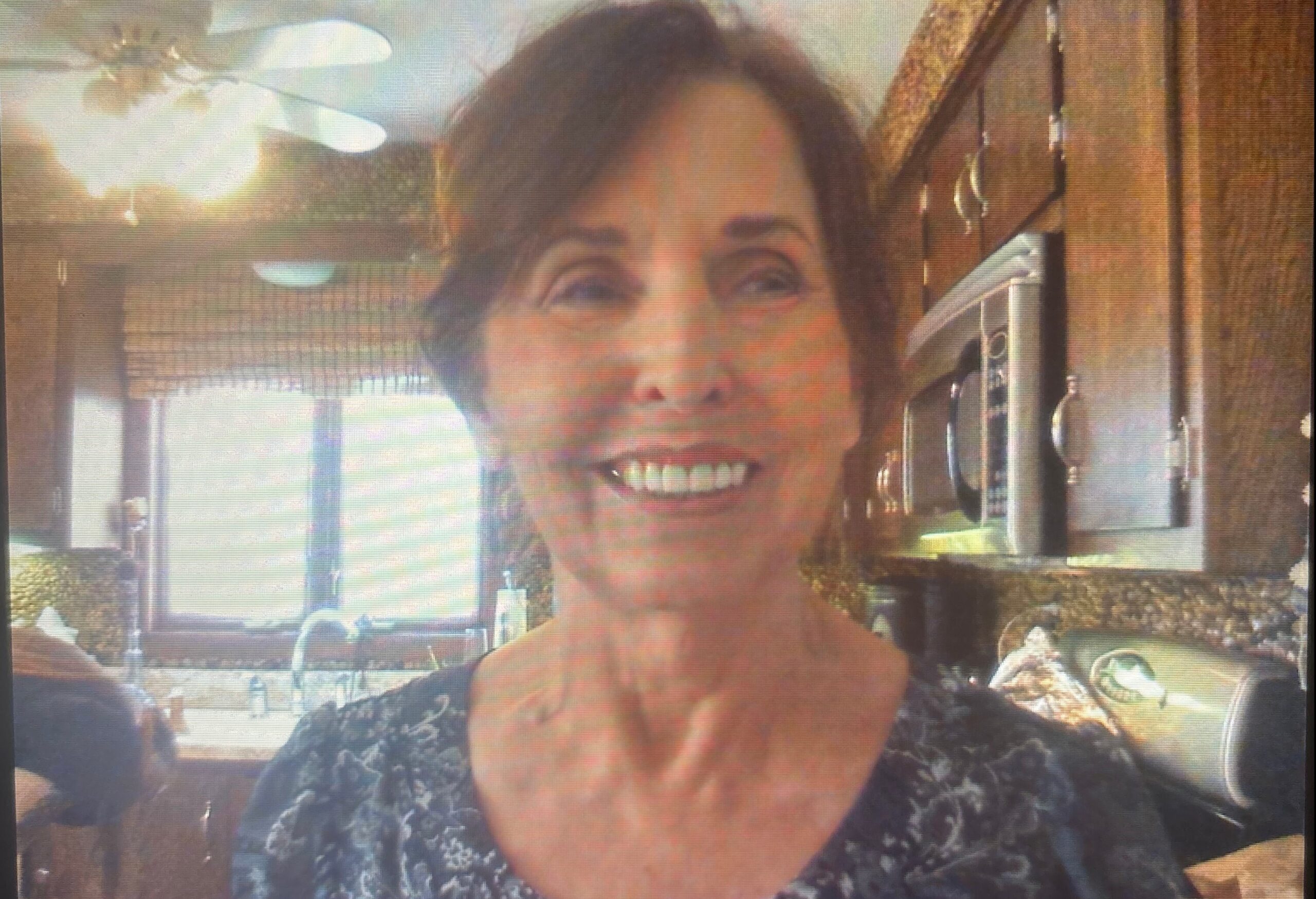 Smiling woman taking a selfie in a kitchen with wooden cabinets and appliances in the background.
