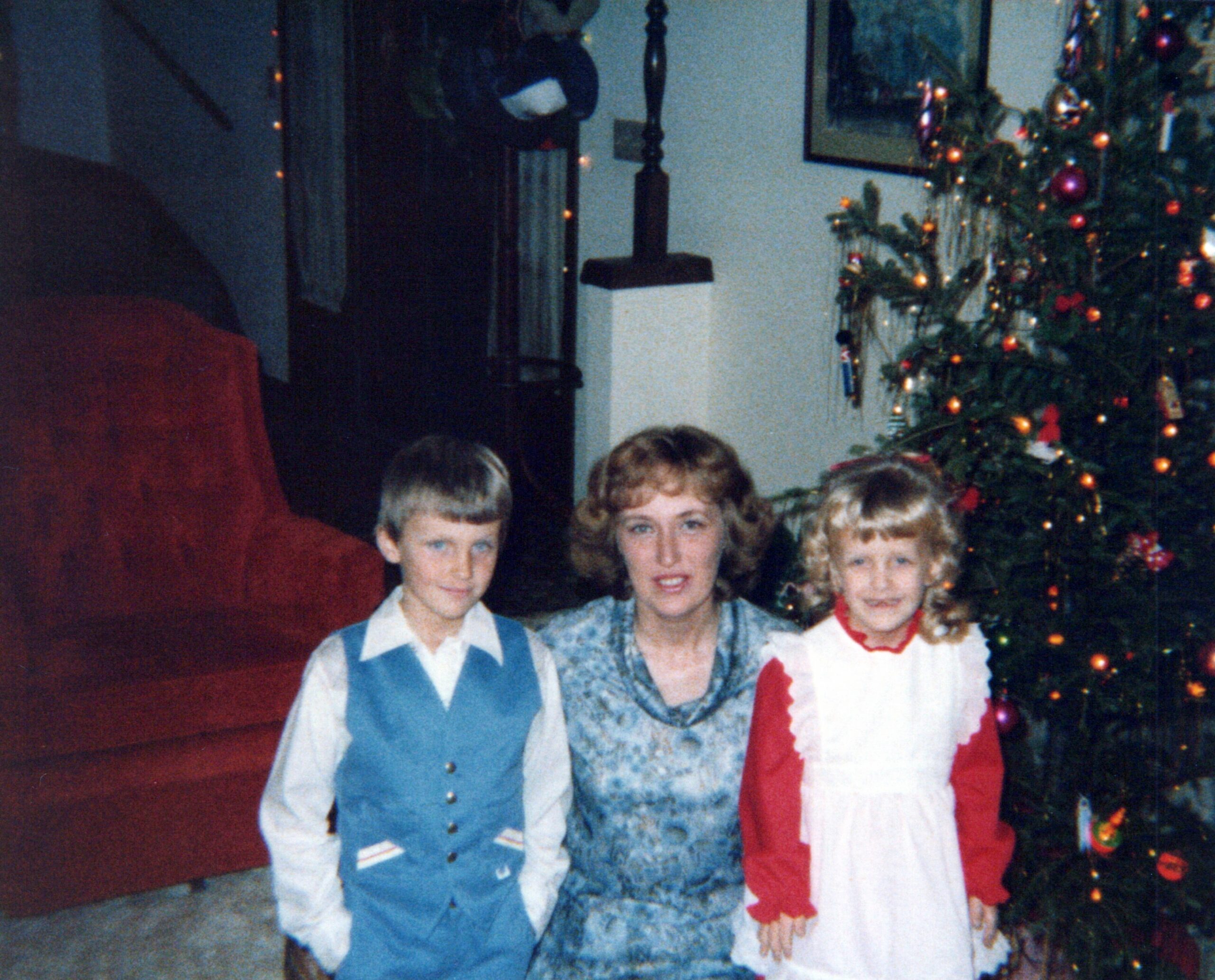 Family posing for a Christmas photo indoors, wearing festive clothes with a decorated tree in the background.