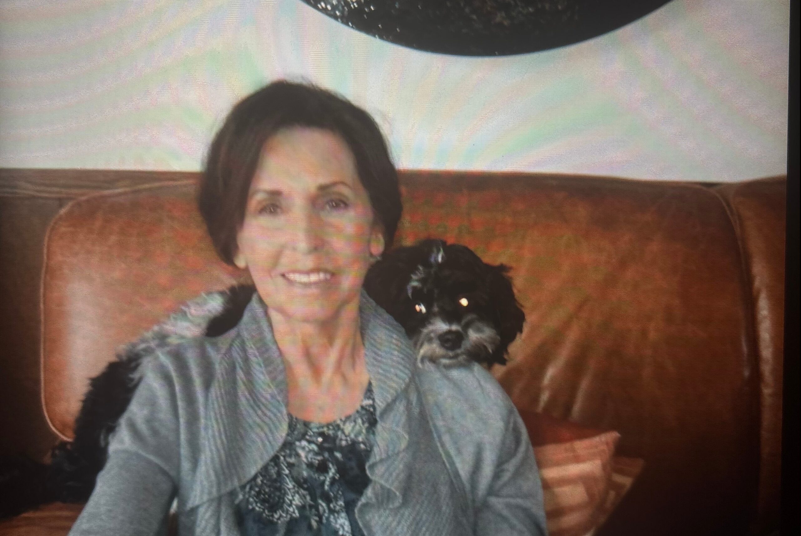 Smiling woman sitting on a brown leather couch with a small black dog by her side.