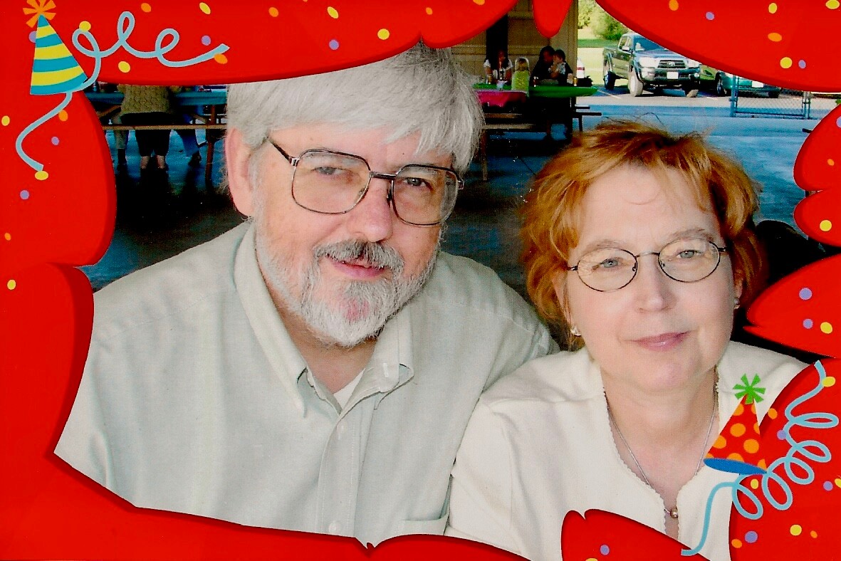 Smiling elderly man and woman pose together, framed by a red birthday prop with confetti at an outdoor gathering.