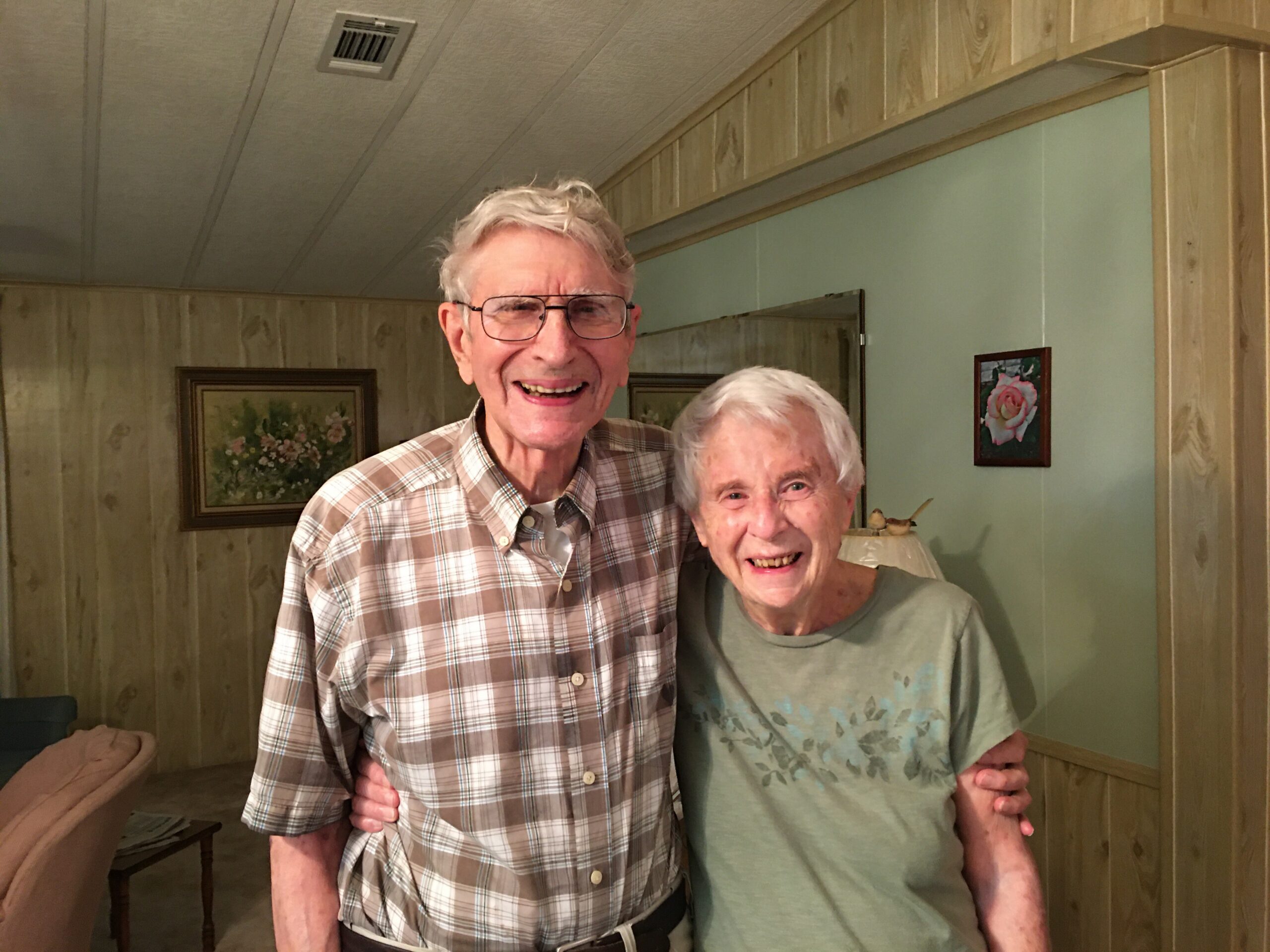 Two smiling elderly people posing together in a wood-paneled room.