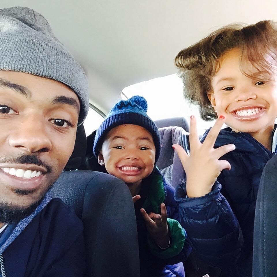 Man and two children in a car, smiling at the camera for a selfie.