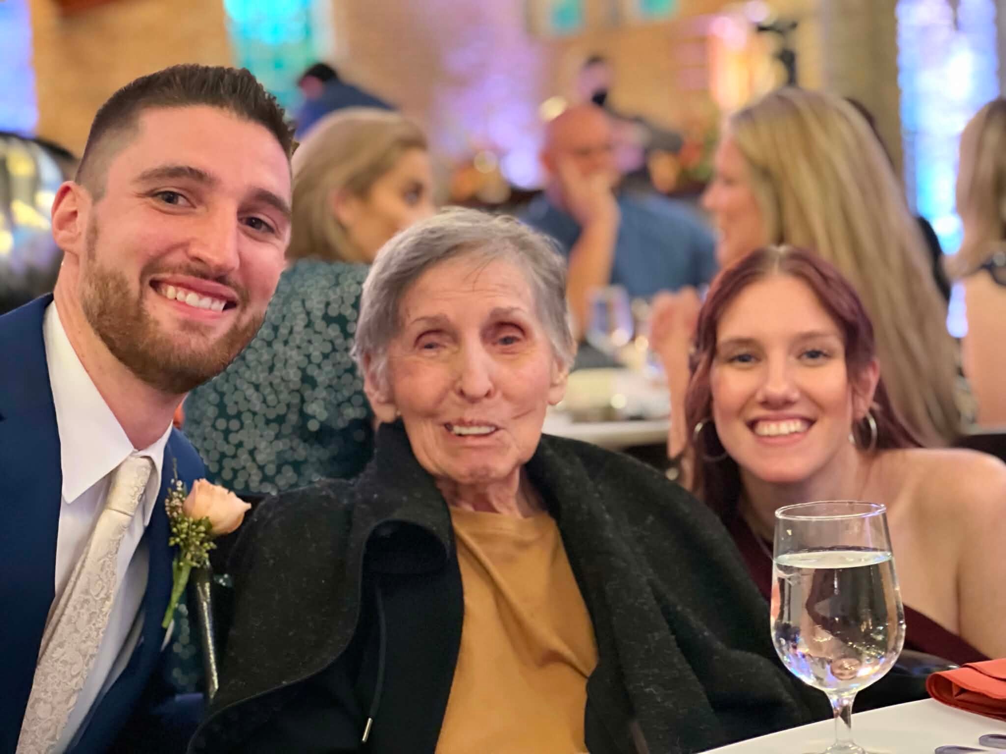 Three people smiling for a selfie at a celebratory event, with a wine glass in the foreground.