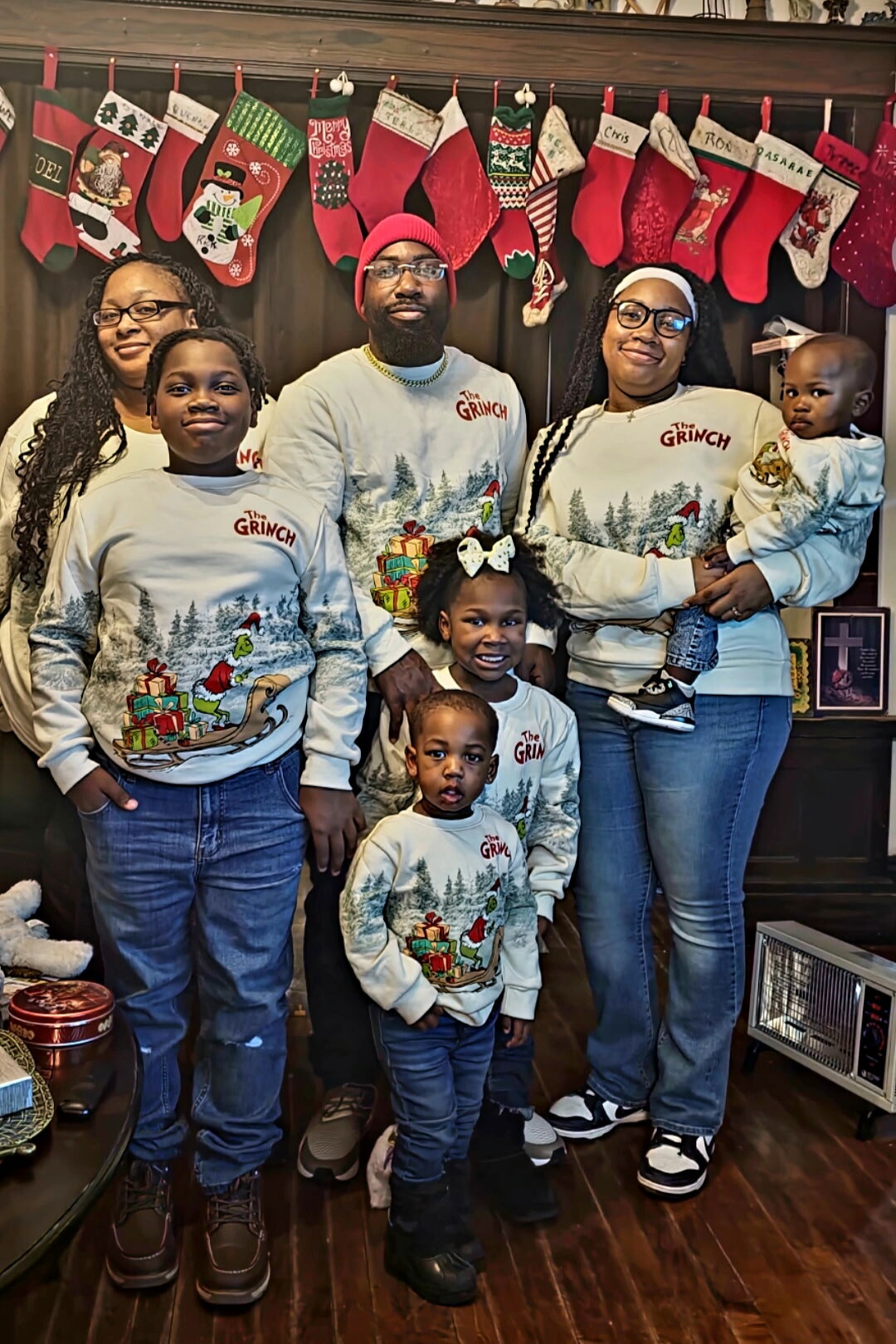 Family of six in matching The Grinch Christmas sweaters posing in a living room with red stockings above the hearth.