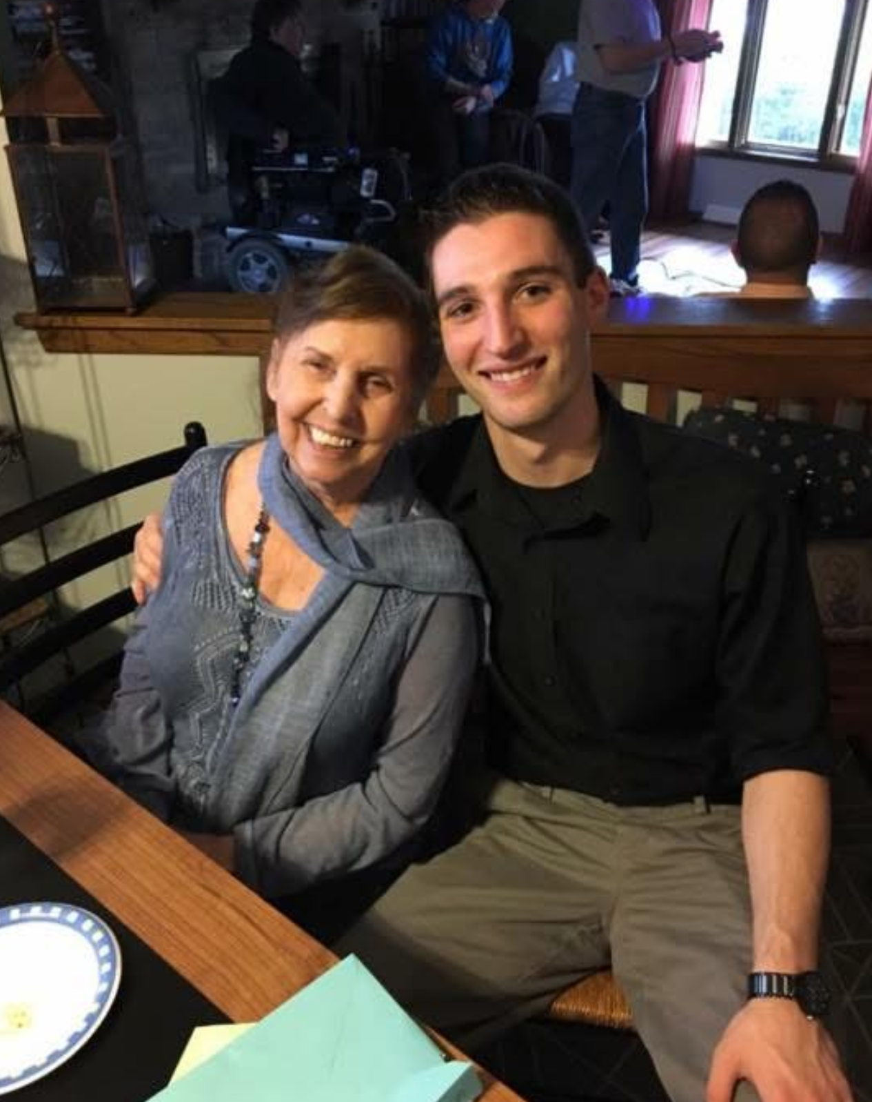 Smiling woman and young man sit side by side at a wooden table in a restaurant, posing for a photo together.