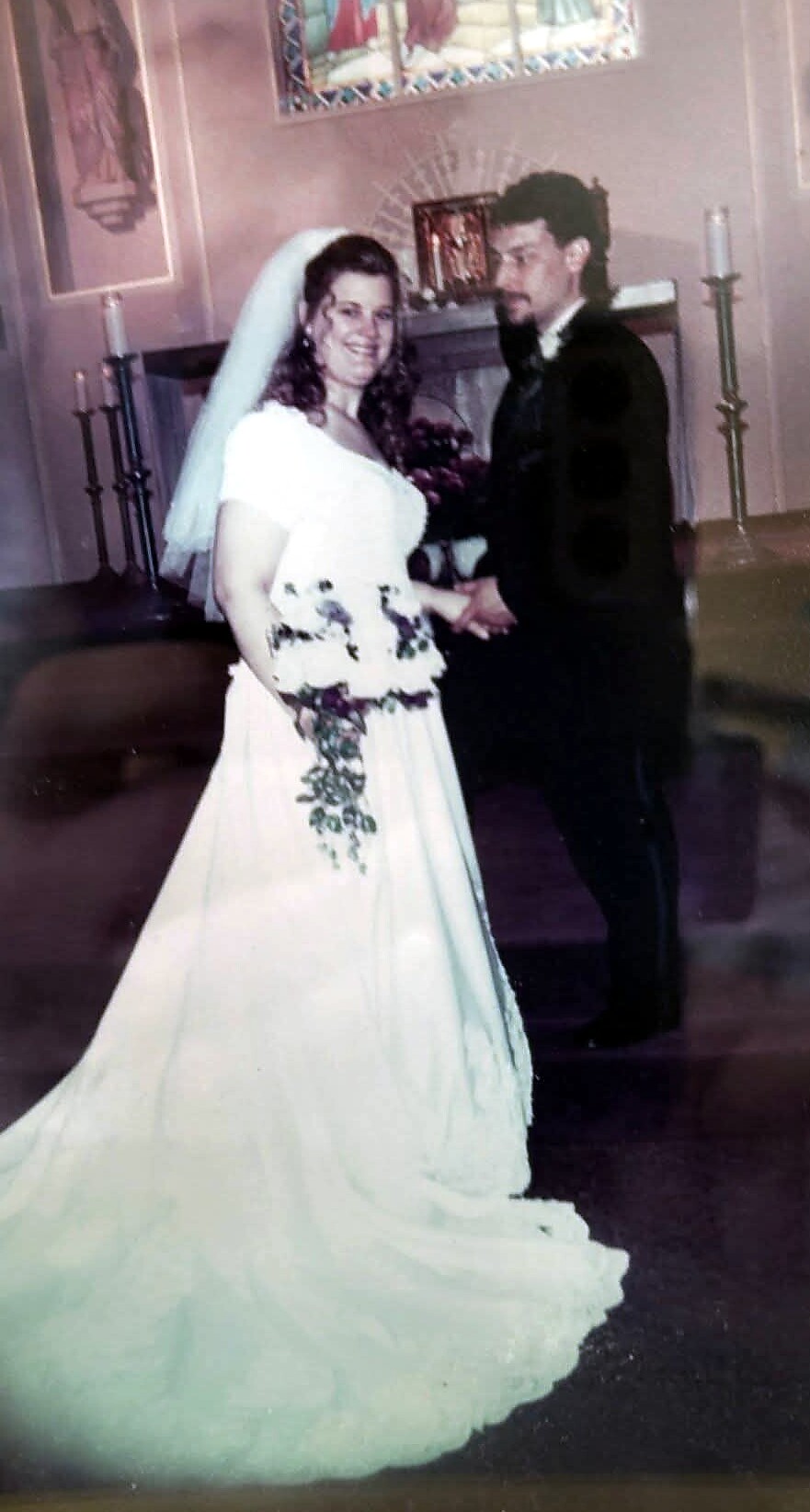 Bride in a white wedding gown and veil stands with groom in a dark suit inside a church.