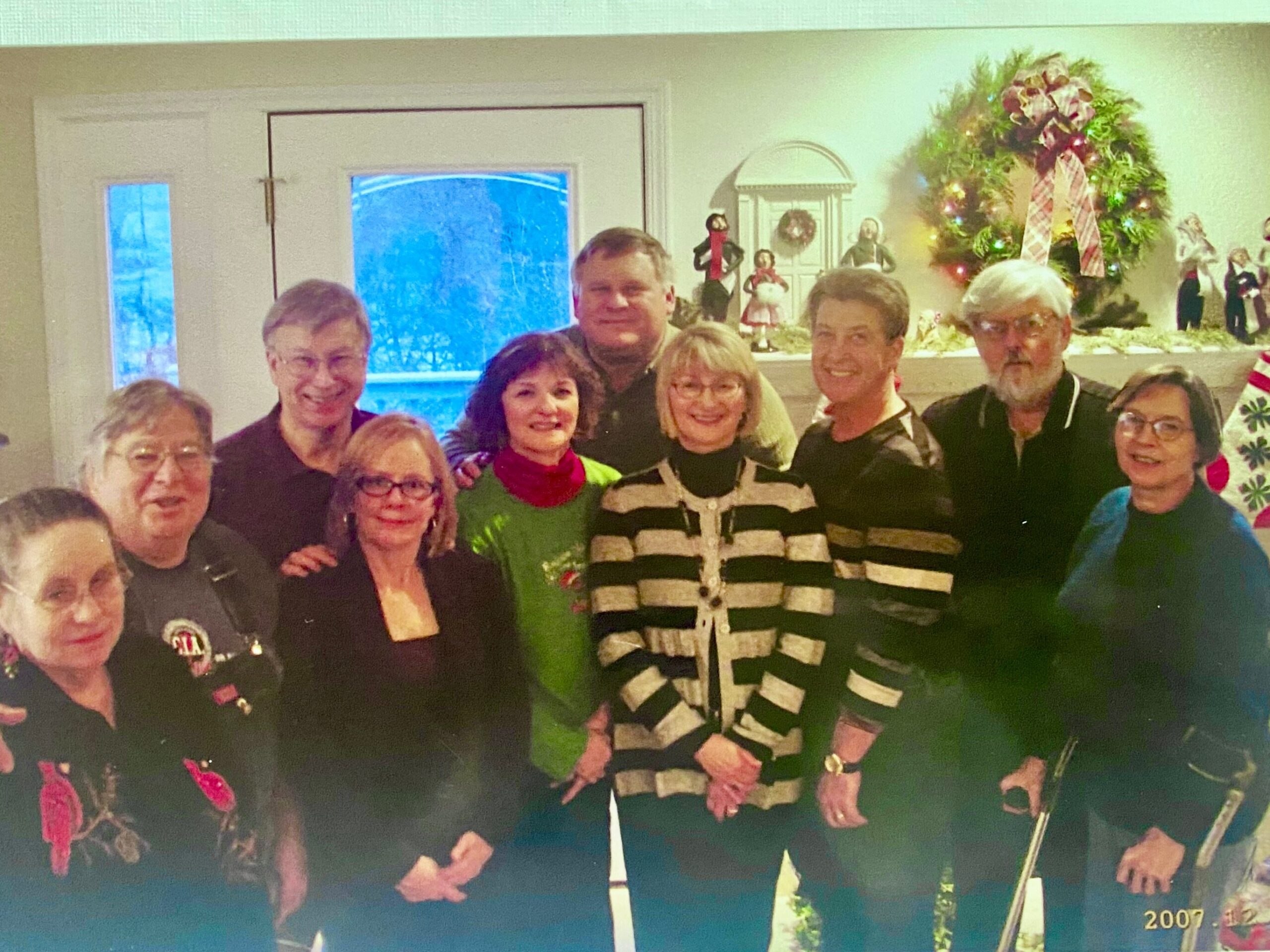 Group of adults posing for a Christmas gathering indoors, decorated with a large wreath in the background (2007).